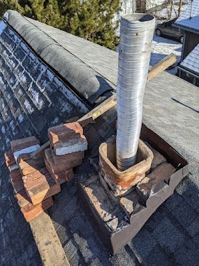 Roof chimney flashing with metal vent pipe, bricks, and shingles on a rooftop
