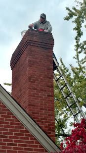 Person on top of a red brick chimney using a ladder, working on the roof