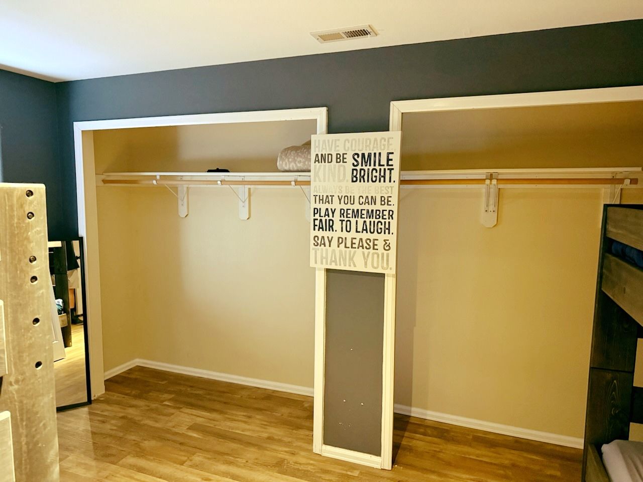Empty walk-in closet with wood floors, white shelves, and a hanging sign on the back wall.