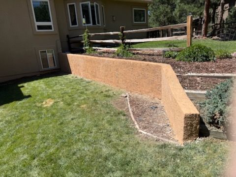 Curved orange retaining wall beside a grassy yard and house in a landscaped backyard