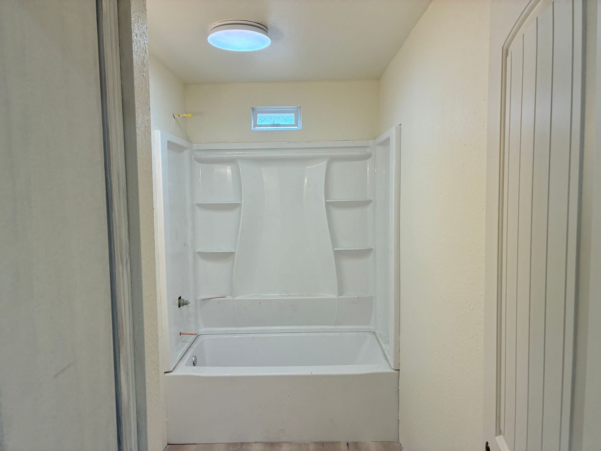 Empty cream-colored bathroom with a white bathtub/shower alcove and a small window above it