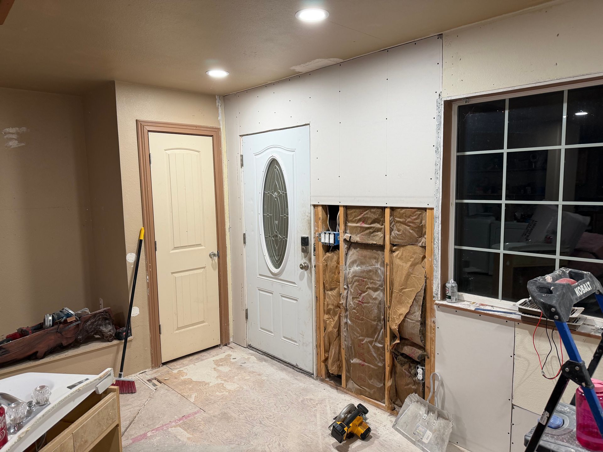 Partially renovated room with exposed wall studs, a white door, window, and tools on the floor