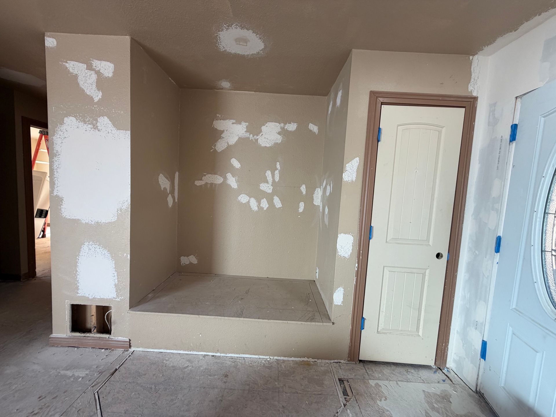 Empty unfinished room with patched tan walls, a closet nook, and white and blue doors.