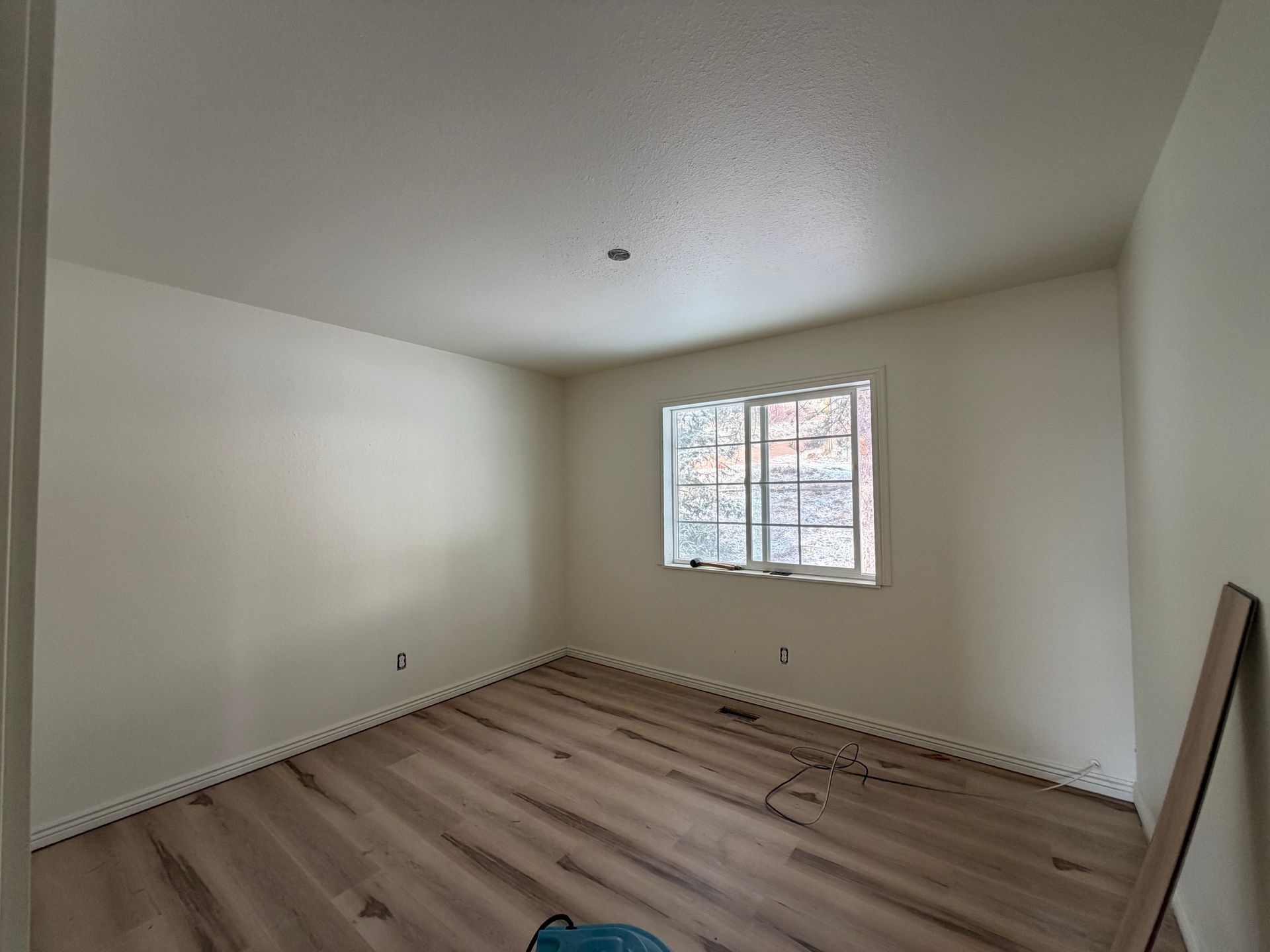 Empty unfurnished bedroom with light wood flooring, white walls, and a small window.