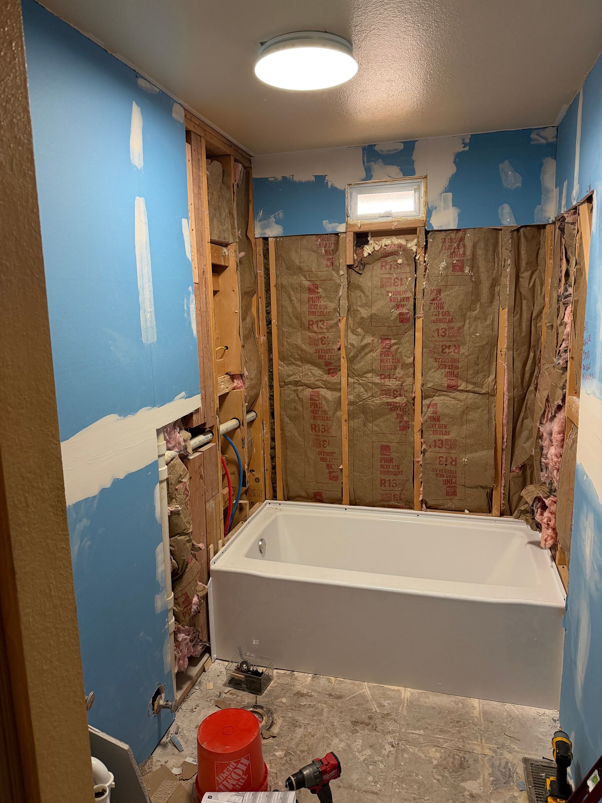 Bathroom under renovation with exposed insulation and a white bathtub beneath blue walls.