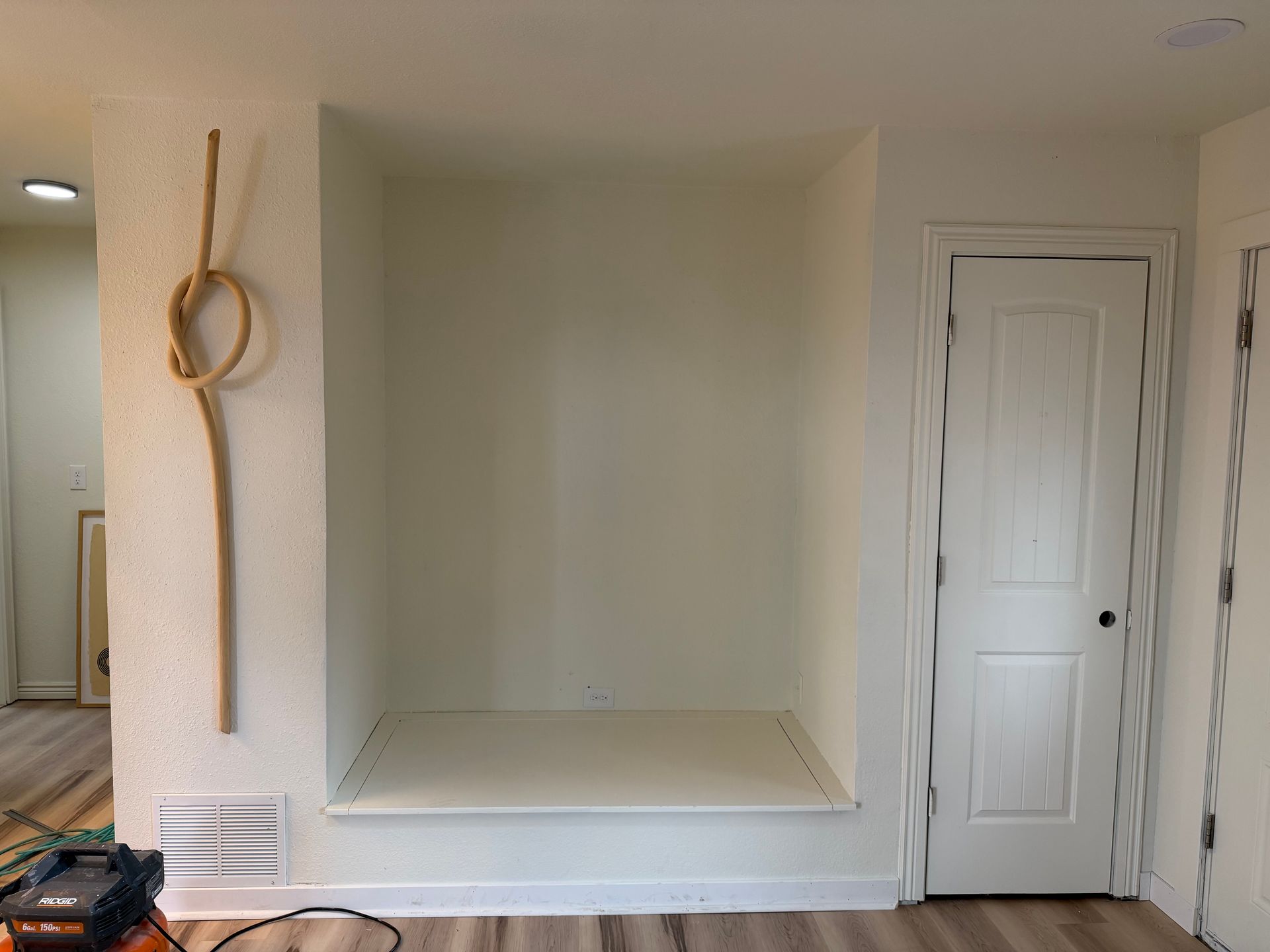 Empty recessed wall niche with white trim beside a closed white door and hanging rope decor