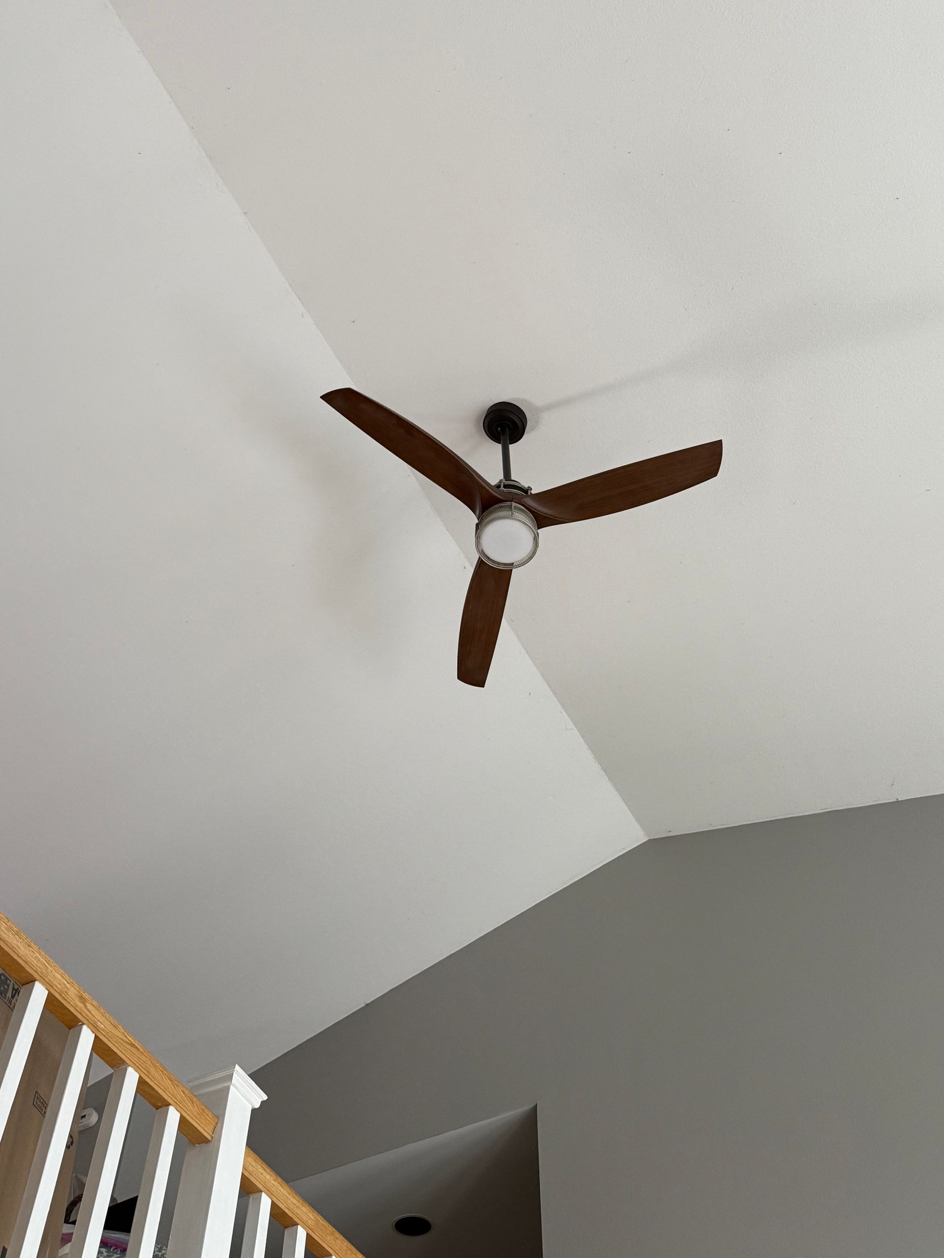 Ceiling fan with dark wood blades on a white vaulted ceiling above a stairwell