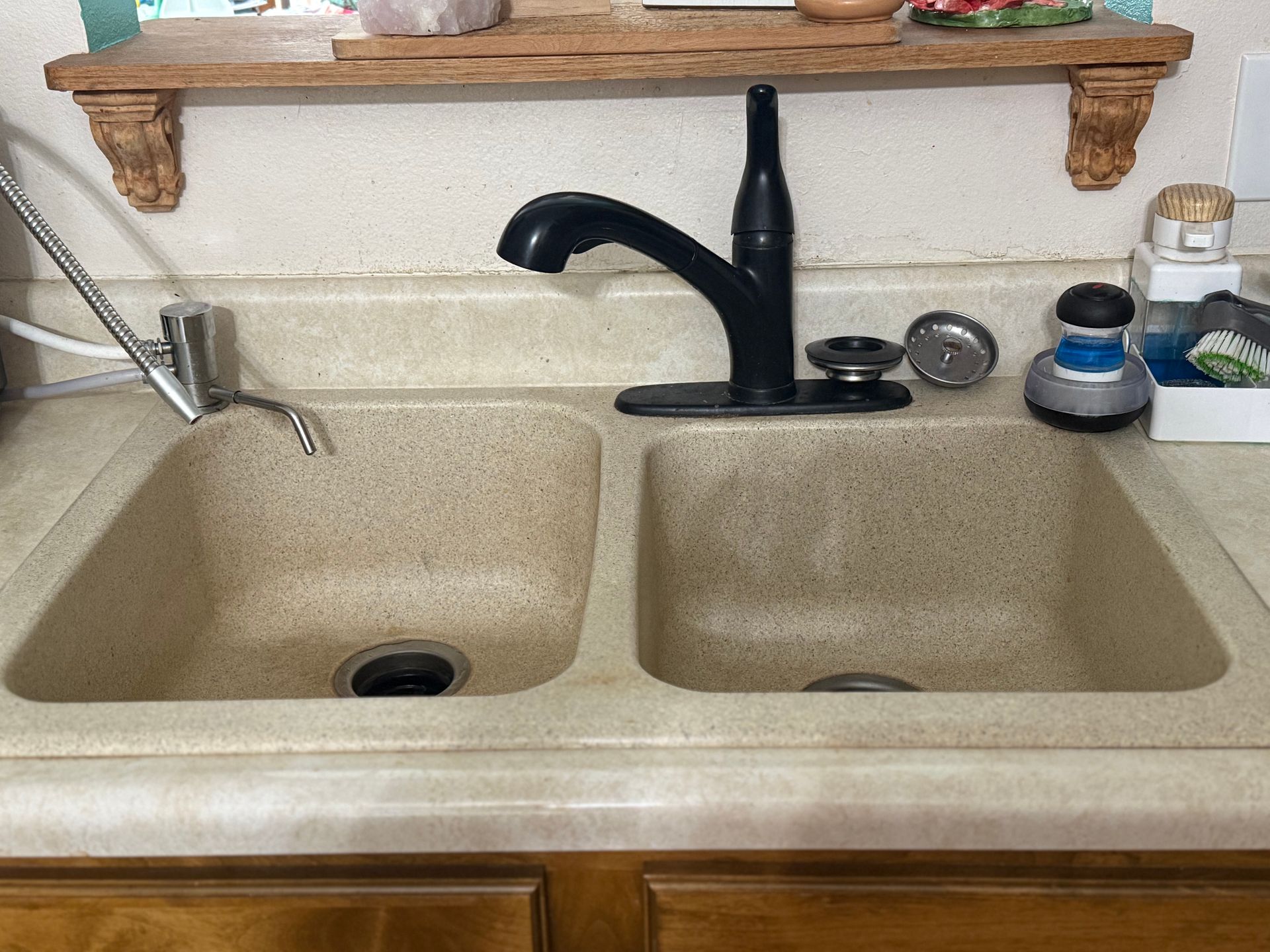 Kitchen sink with beige double basins, black faucet, and cleaning supplies on the right counter