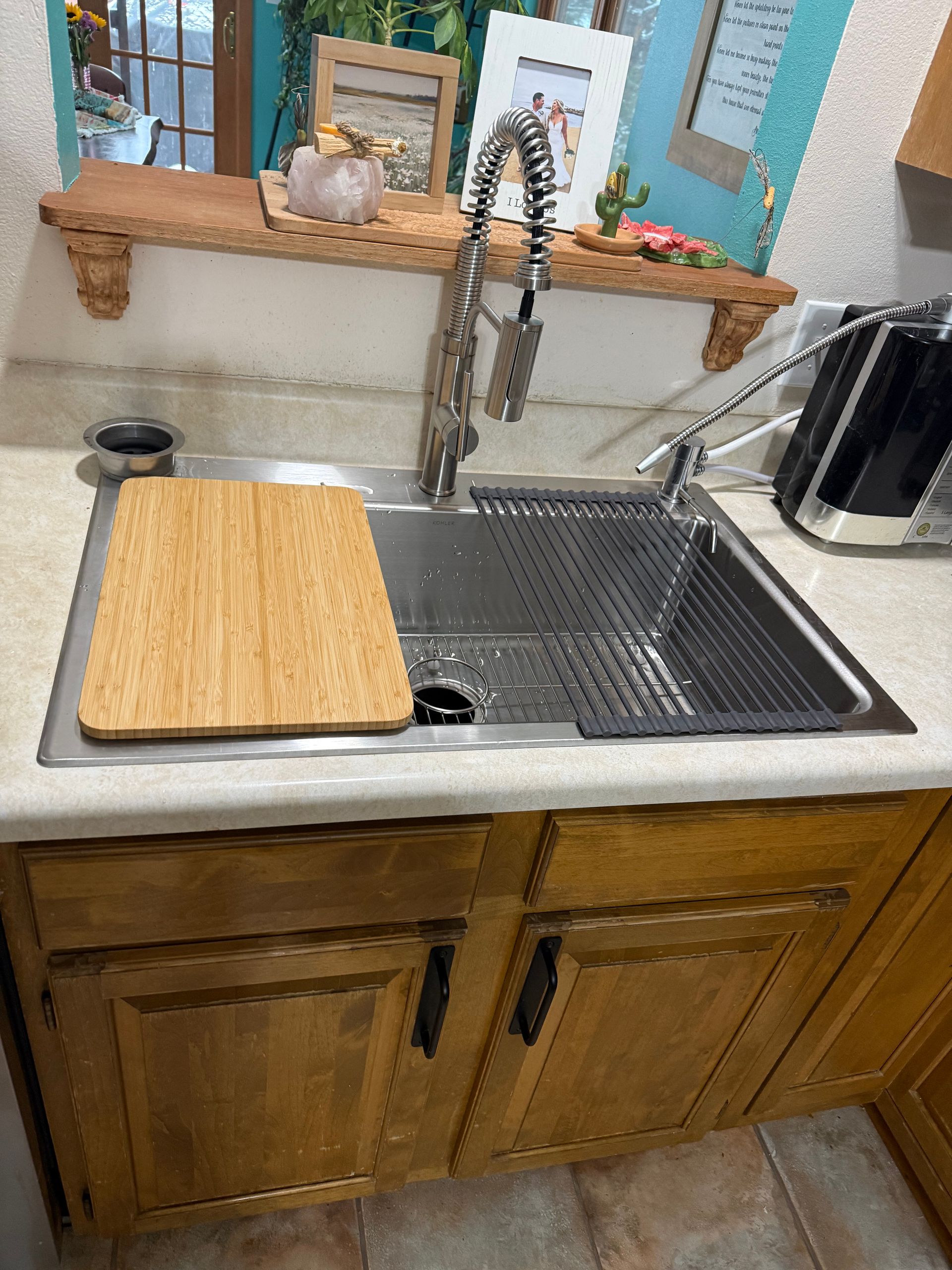 Kitchen sink with drying rack, wood cutting board, soap dispenser, and wooden cabinets beneath a window.