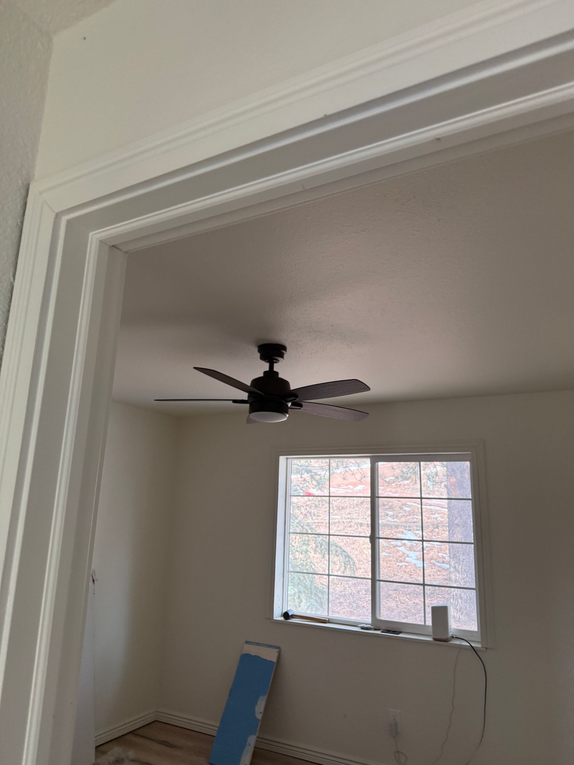 Empty room with ceiling fan, window, and paint tools near the wall