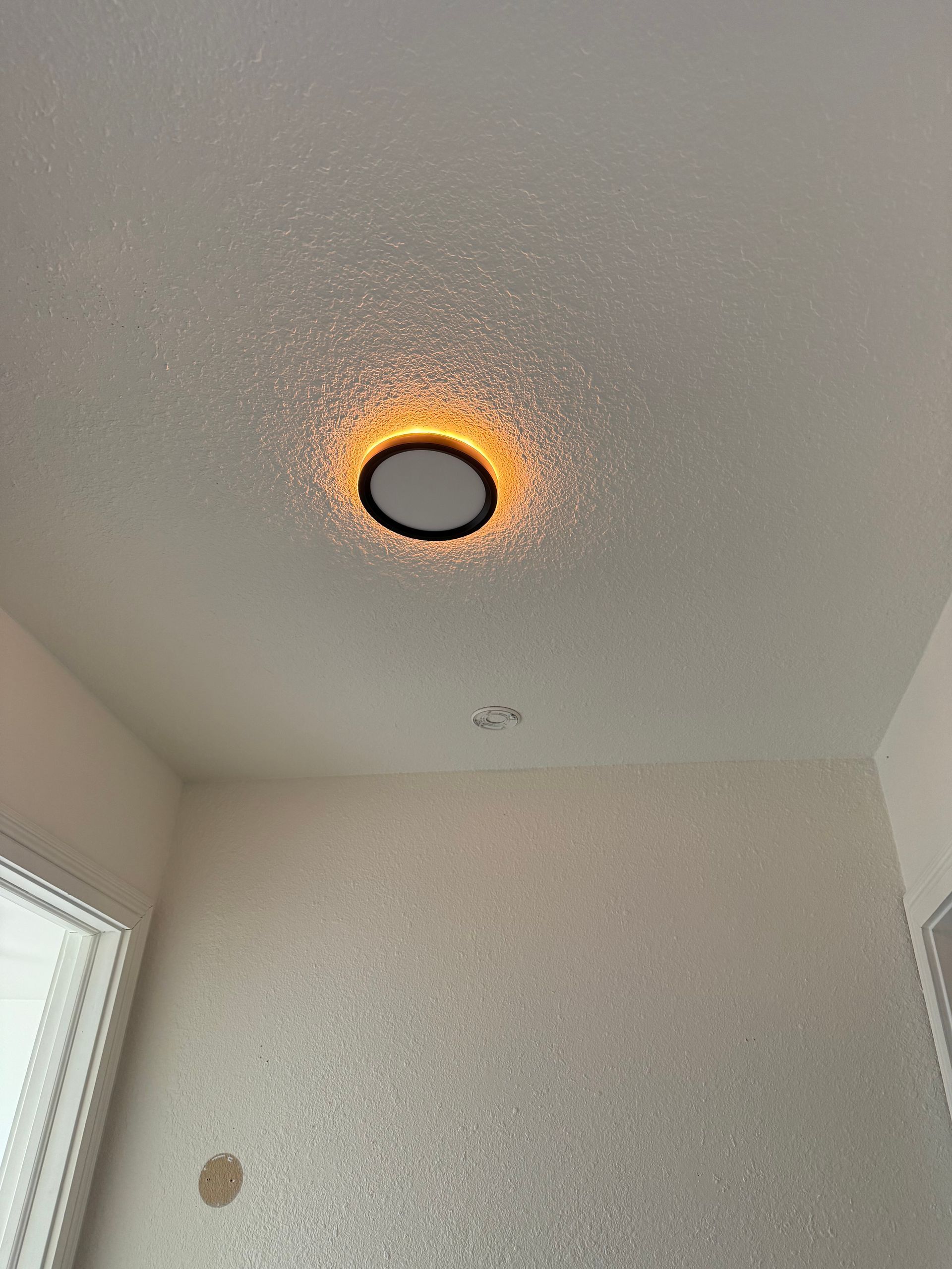 Ceiling with a round light fixture glowing orange near the corner of a room