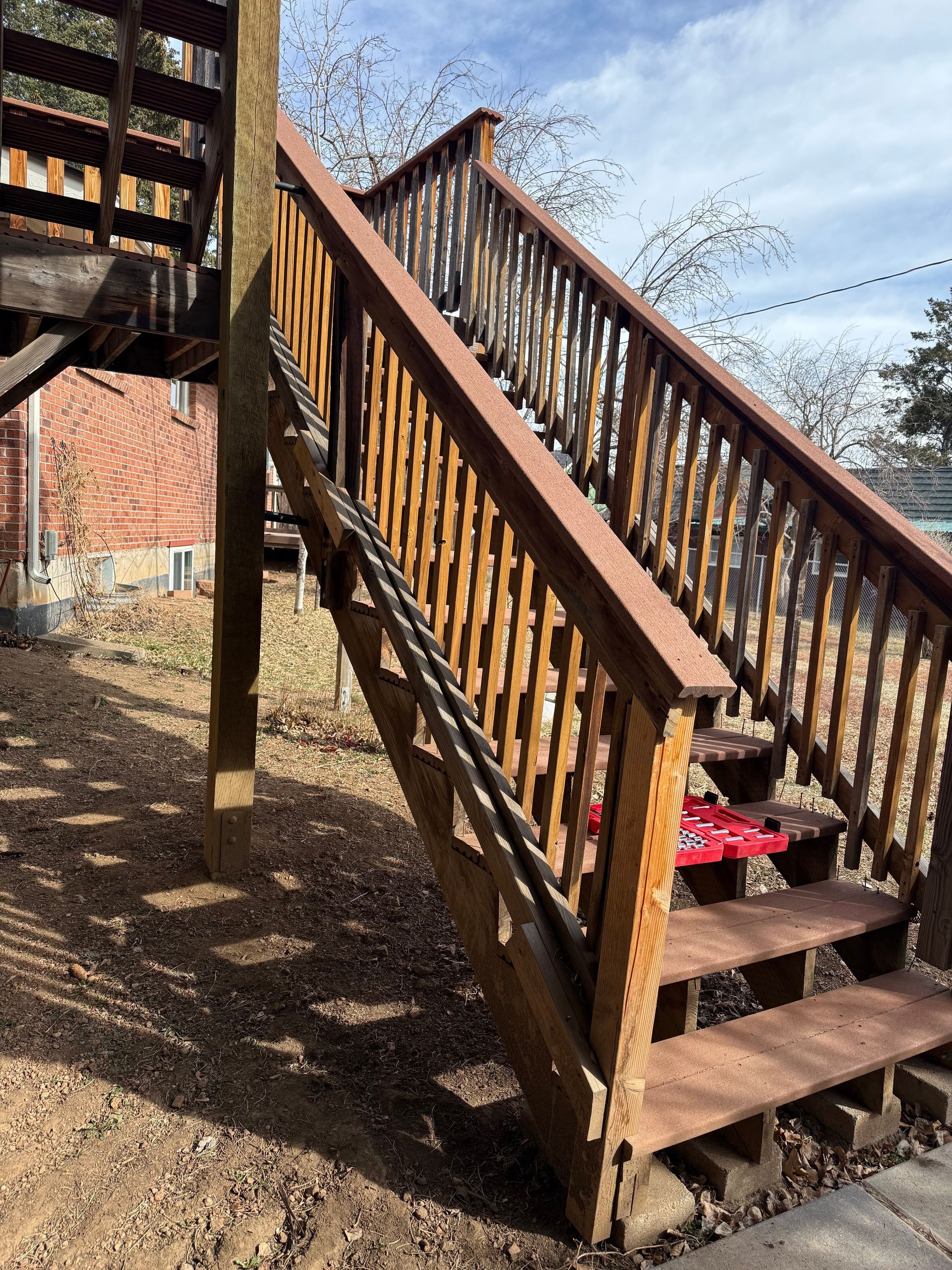 Wooden outdoor staircase with railings beside a brick building on a gravel-covered ground