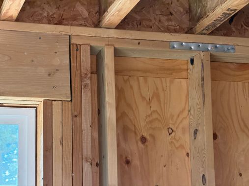 Framed wooden wall with exposed studs and a metal bracket under ceiling joists
