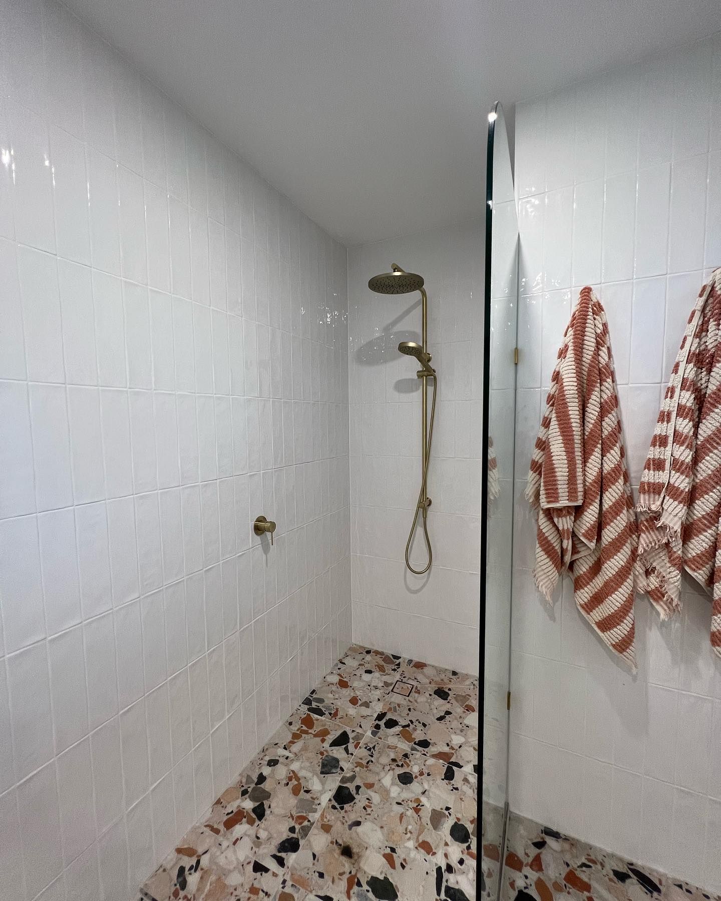 Shower with White Tiled Walls, Patterned Floor and Striped Towels — J & H Plumbing and Gas in Holt, ACT