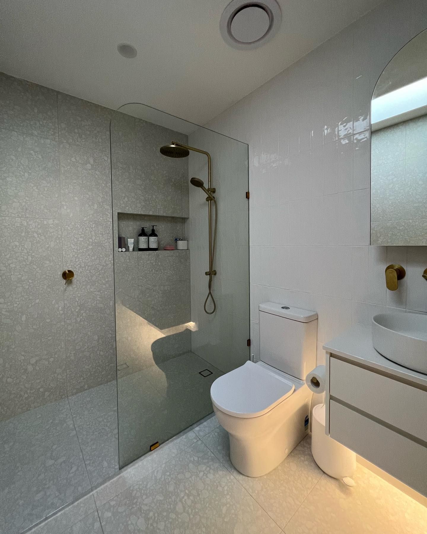 Modern bathroom with grey tiled shower, glass door, white toilet, and gold fixtures — J & H Plumbing and Gas in Holt, ACT
