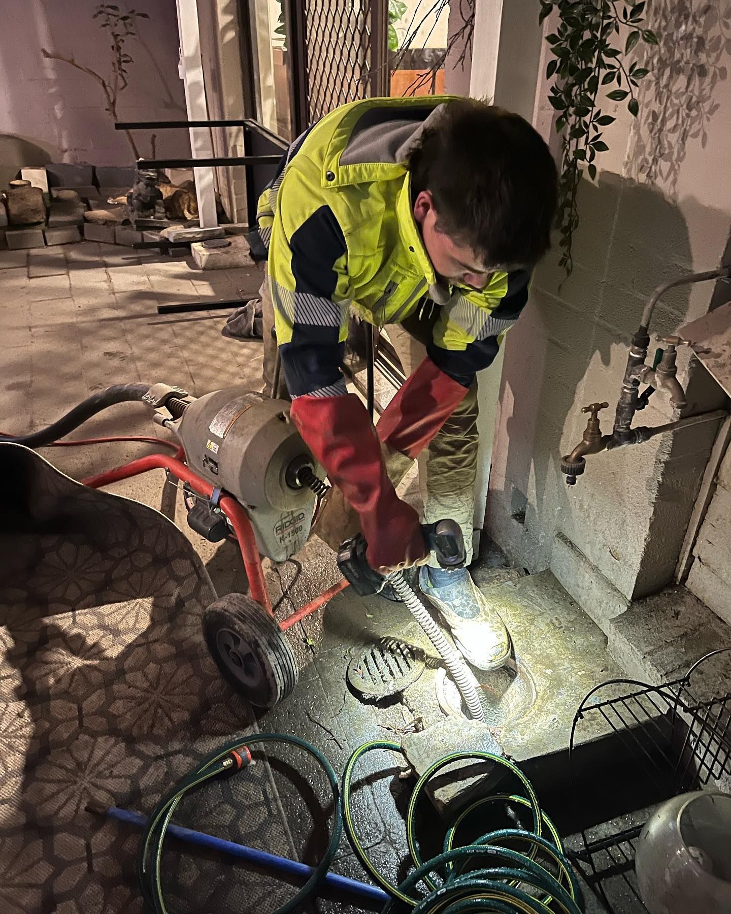 Plumber Using a Drain Cleaning Machine in A Low-Light Outdoor — J & H Plumbing and Gas in Holt, ACT
