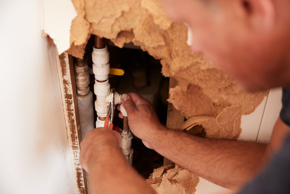 Plumber Using Pliers to Fix Pipes Exposed Inside a Damaged Wall — J & H Plumbing and Gas in Gungahlin, ACT