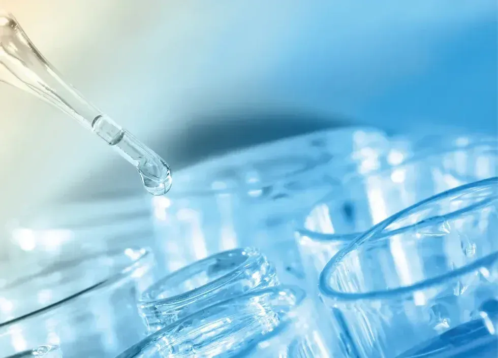Pipette dispensing liquid into clear lab vials on a blue background
