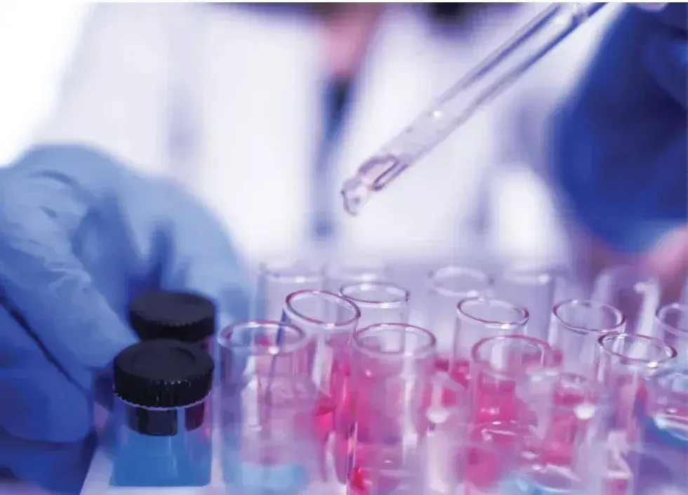 Gloved hands handling test tubes with pink liquid in a laboratory