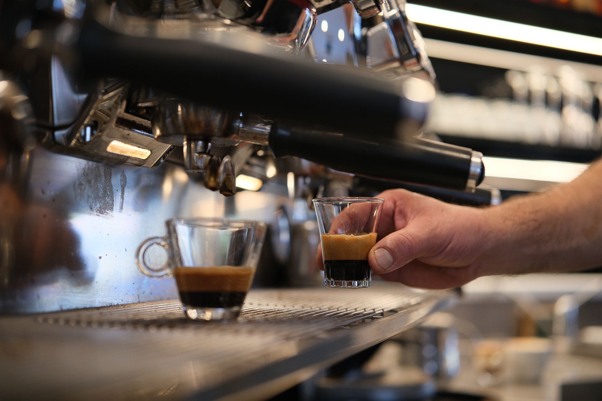 Espresso versato in una piccola tazza di vetro, tenuta in mano vicino alla macchina per l'espresso in un bar.
