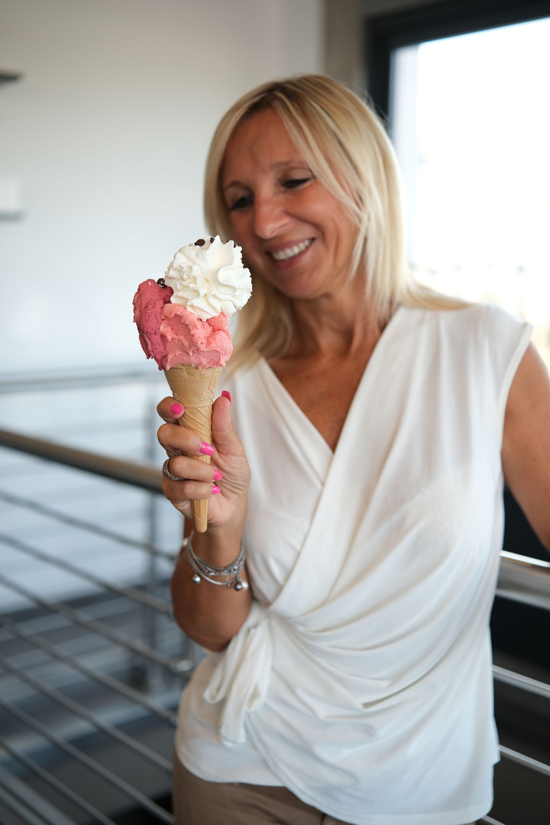 Una donna sorride, tenendo in mano un cono gelato con tre palline, in casa.