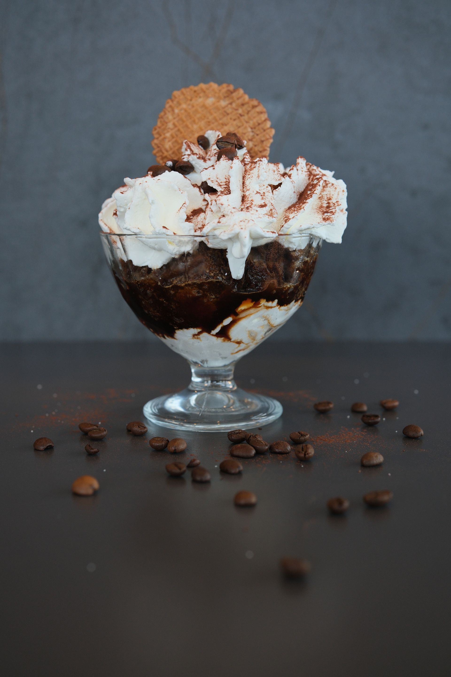 Dessert al caffè con panna montata, cacao in polvere, biscotto waffle, chicchi di caffè in una ciotola di vetro