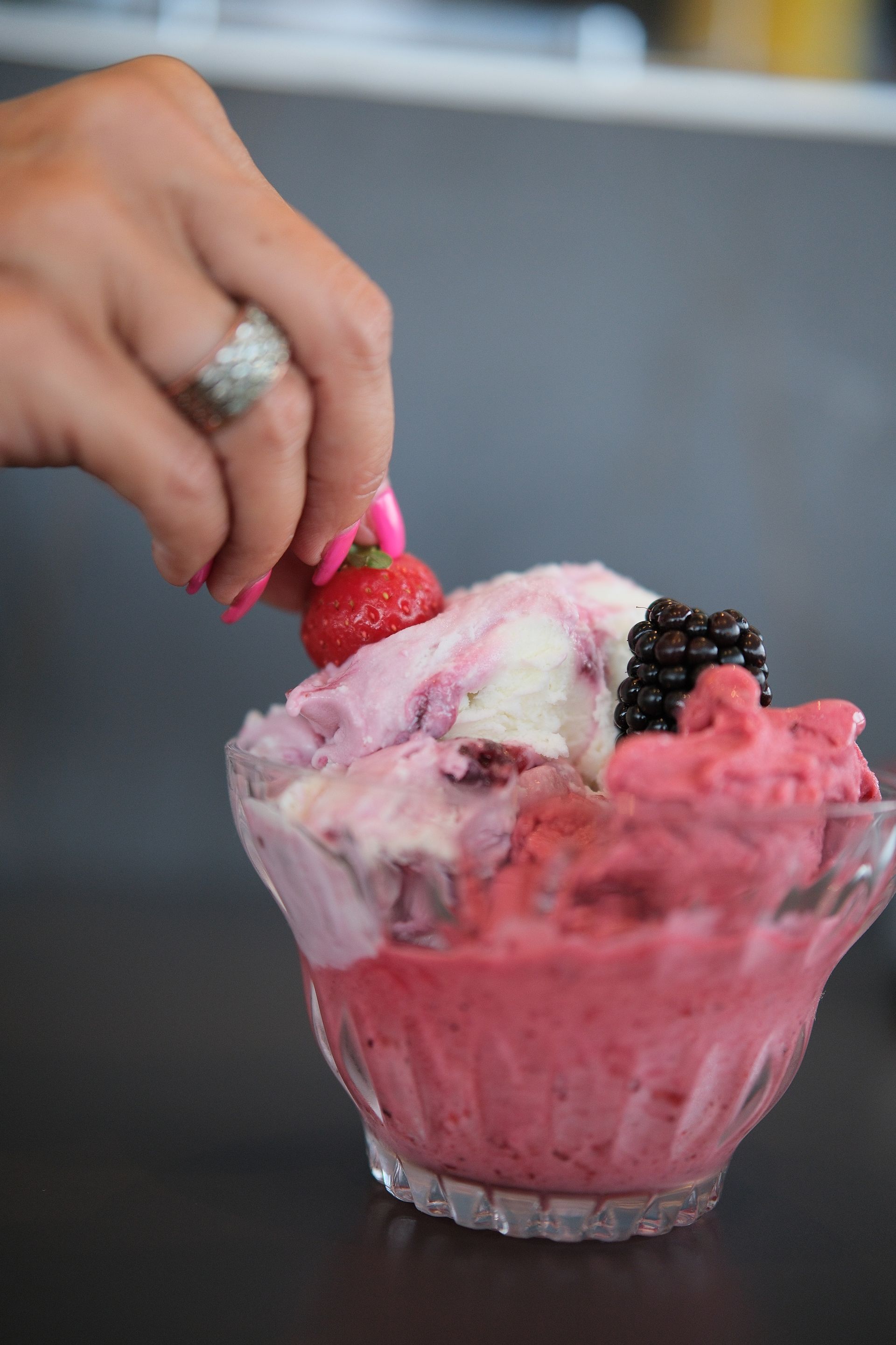 Mano che posiziona una fragola su una coppa gelato ai frutti di bosco in una ciotola di vetro.
