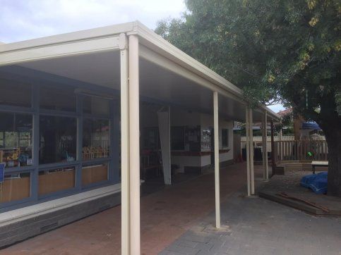 A covered walkway leading to a building with a tree in the background.