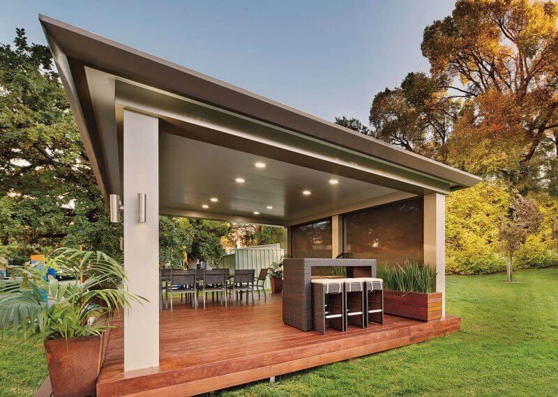 A gazebo with a wooden deck and stools in a backyard.