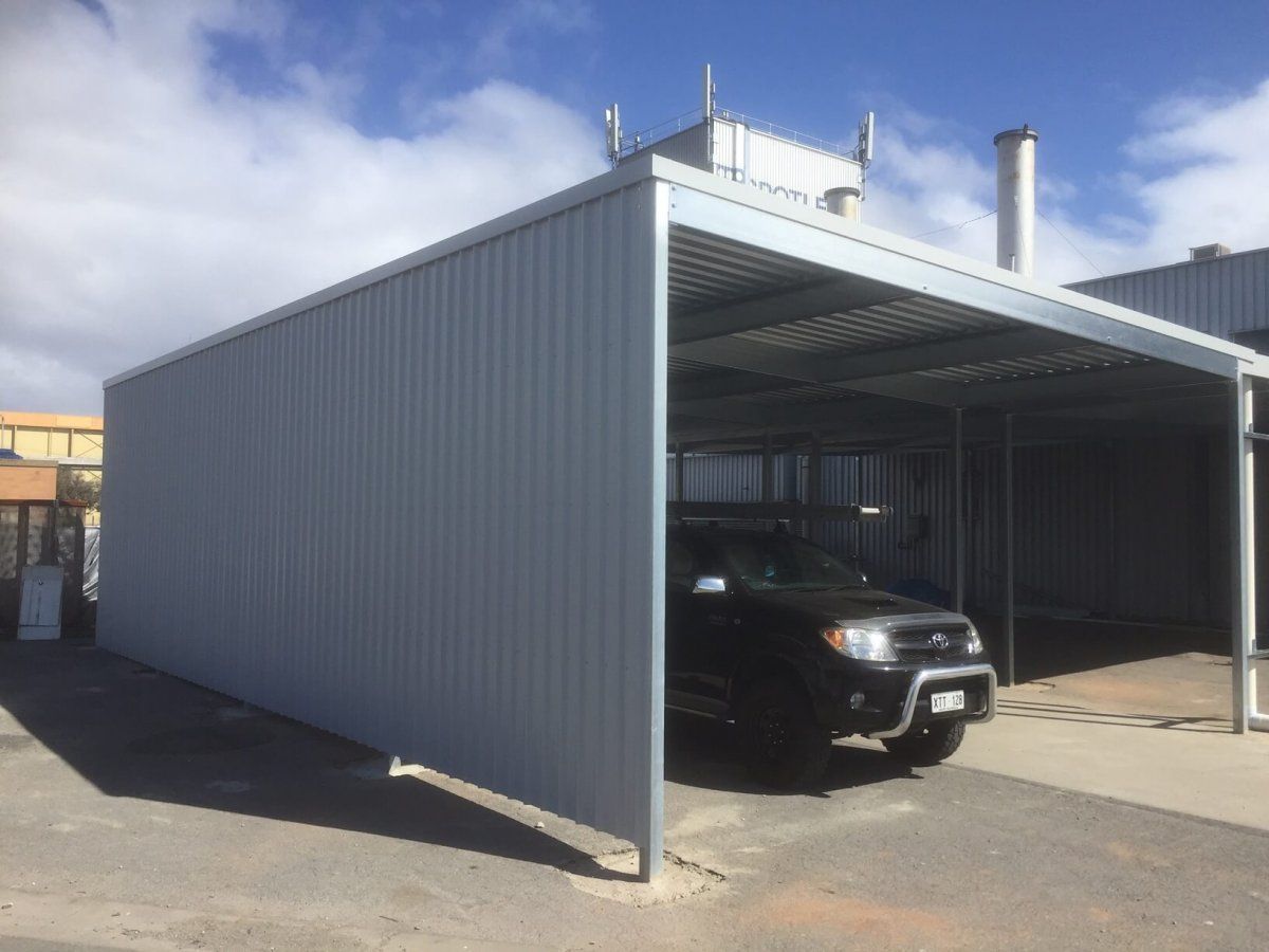 A car is parked under a shed in a parking lot.