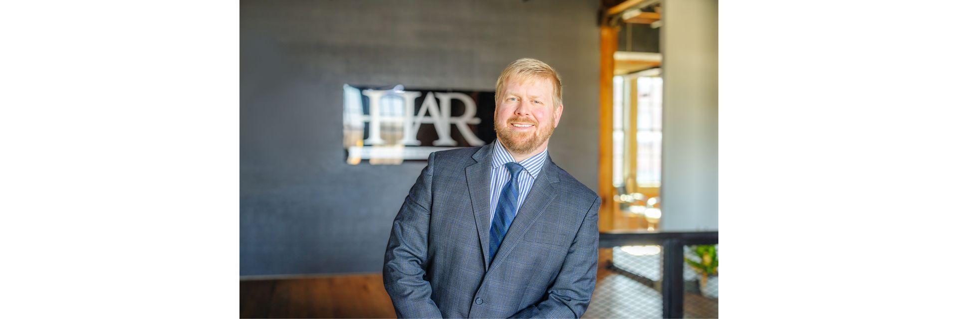 A man in a suit and tie standing in an office in front of a wall with an HAR logo sign.