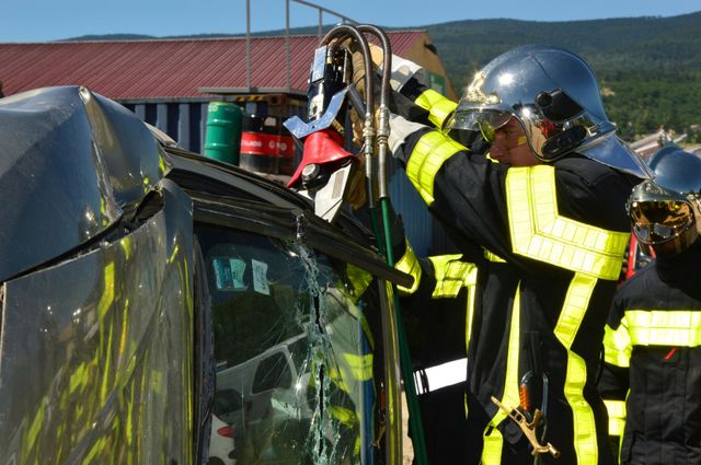 Firefighters in protective gear use hydraulic rescue tools to cut into a damaged vehicle during a rescue operation.