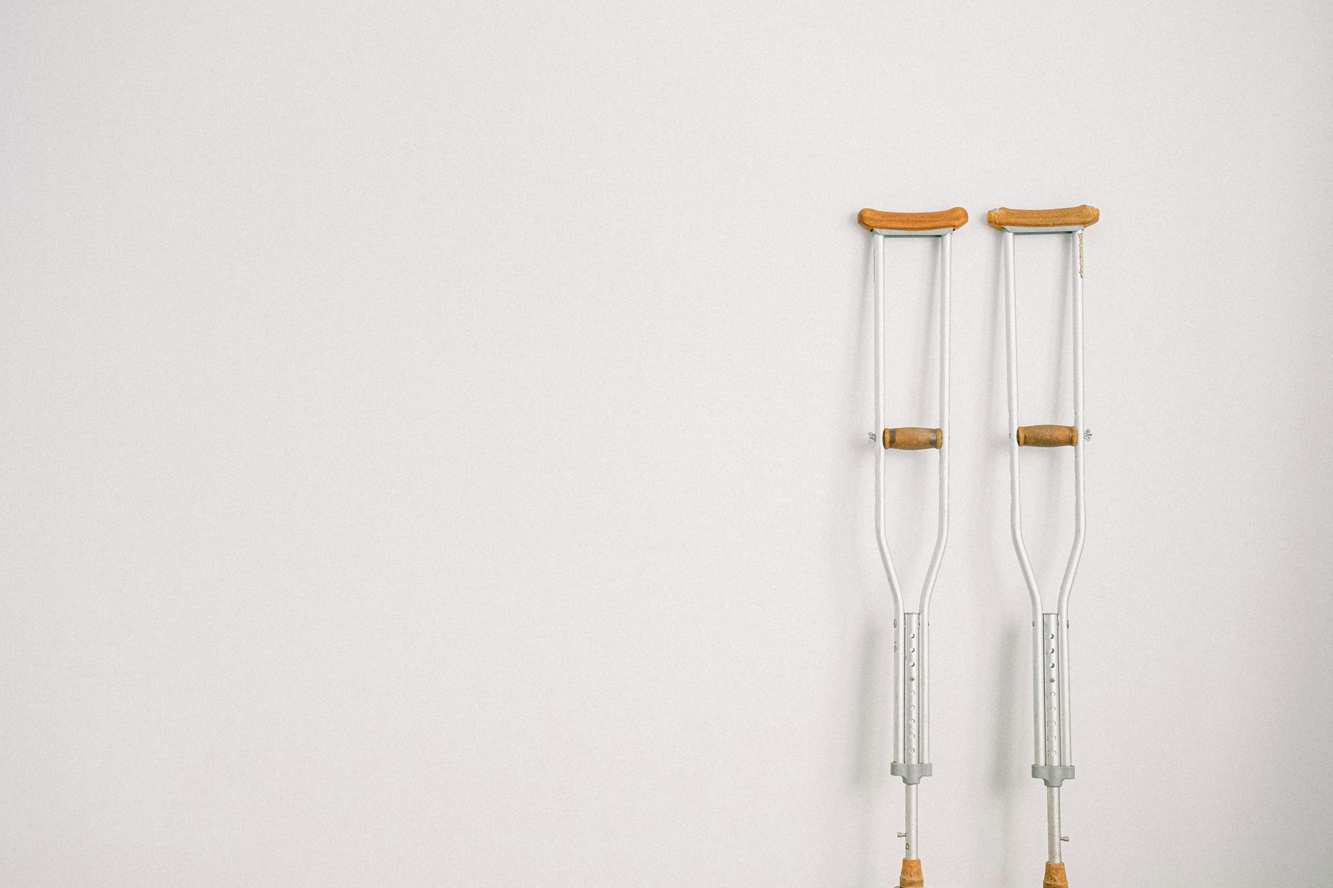 Two metal underarm crutches with wooden handles lean against a plain white wall.