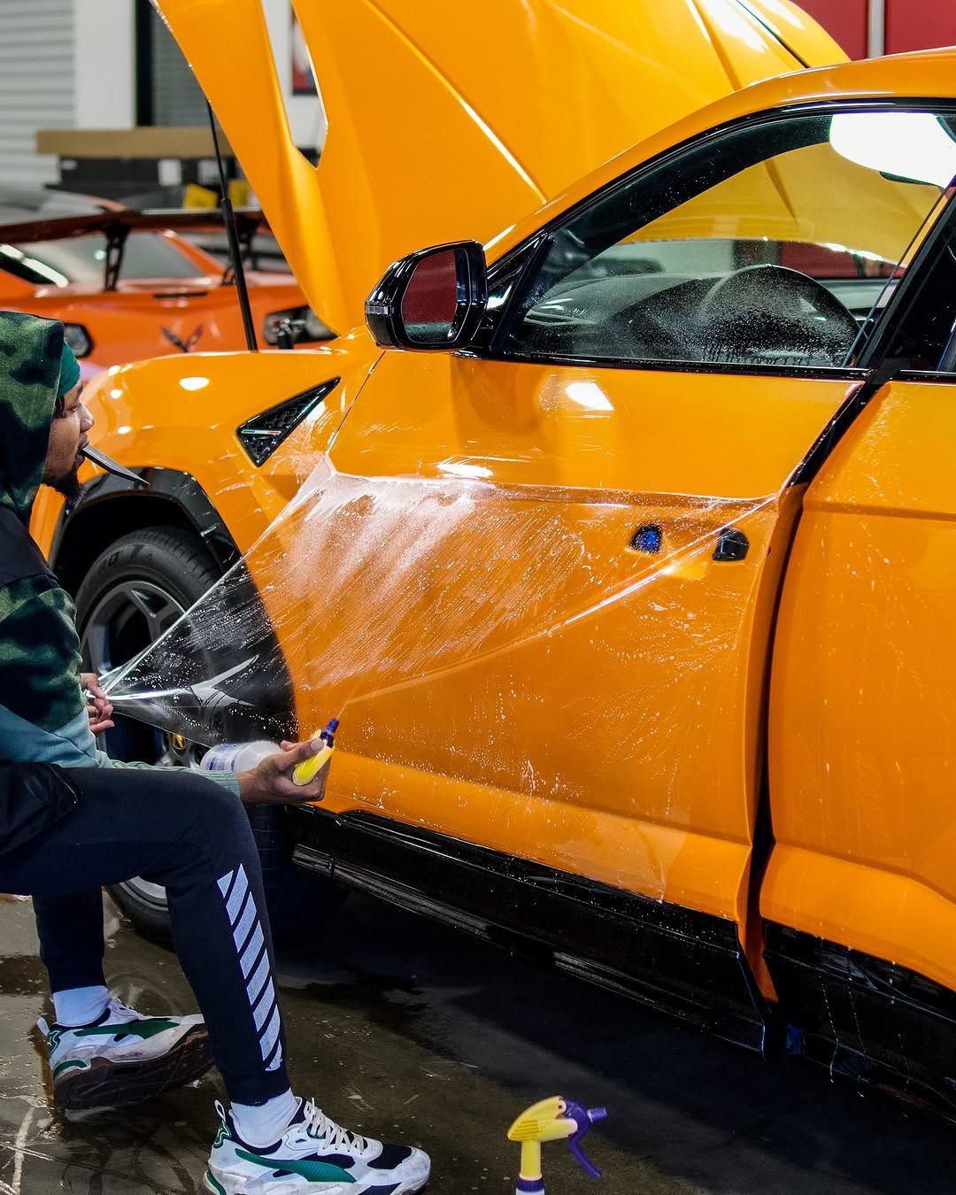 A person is washing a yellow car with a spray bottle