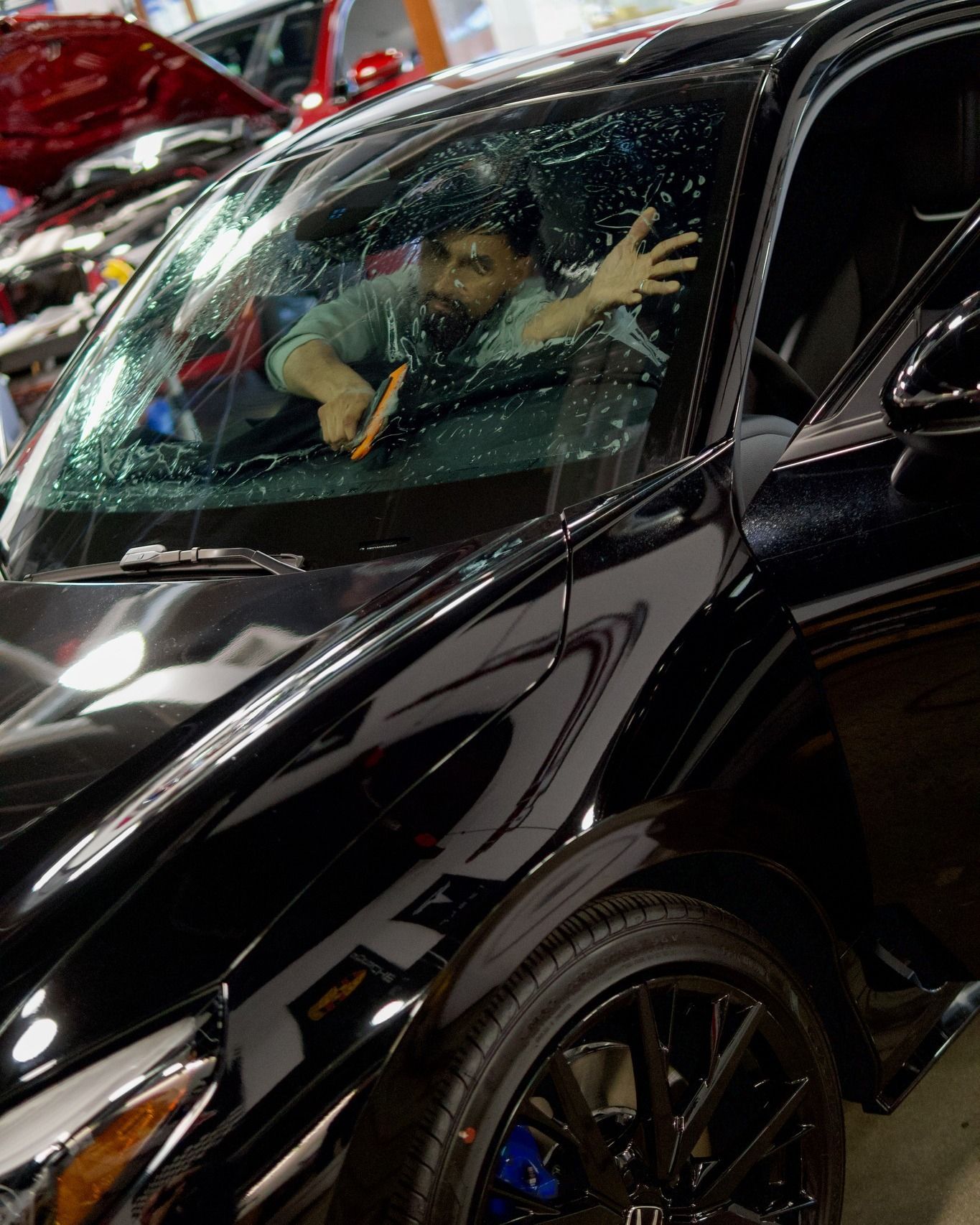 Person inside a black car waving through a rain-speckled windshield in a garage