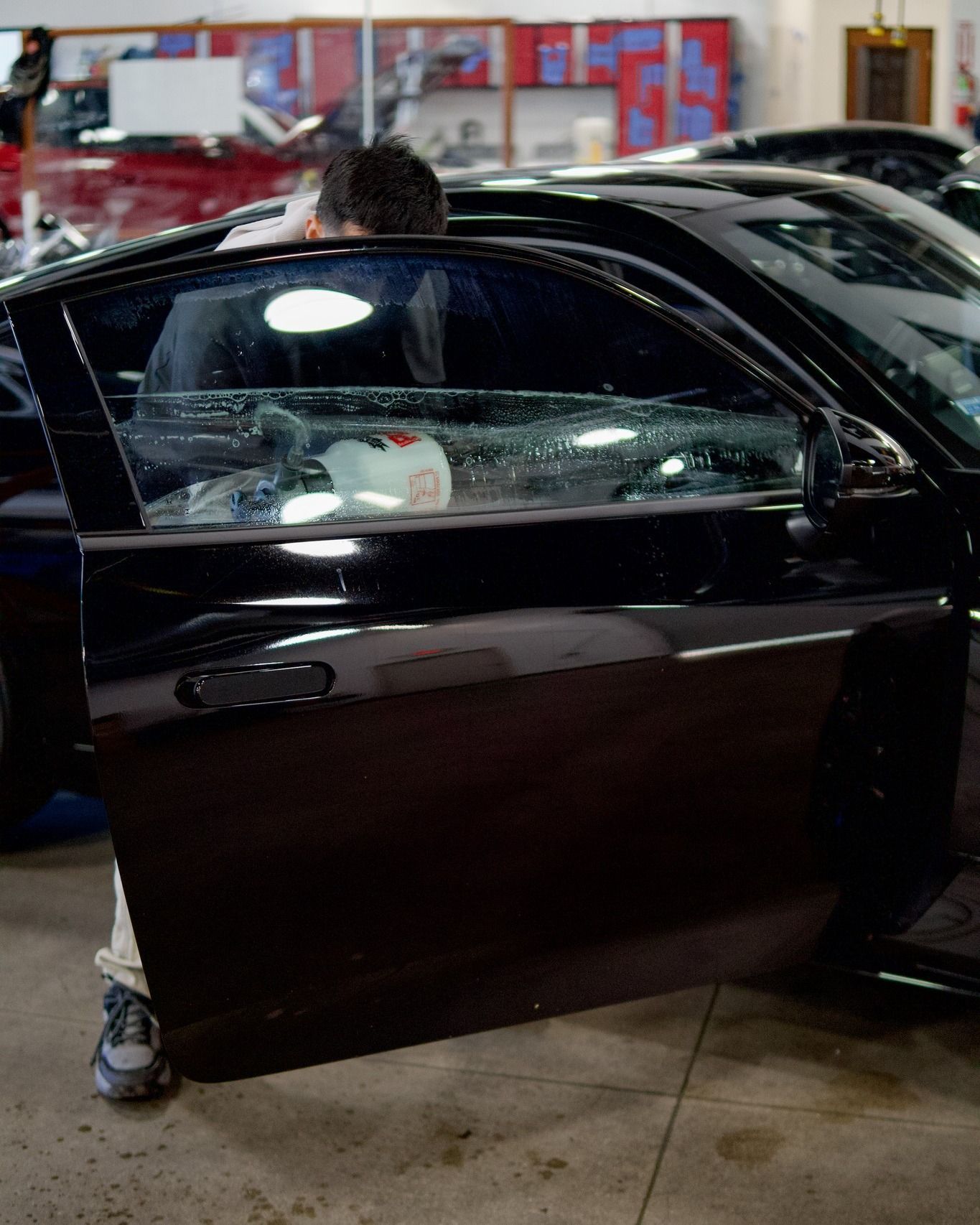 Black car with driver’s door open inside an auto repair shop, with a person standing beside it.