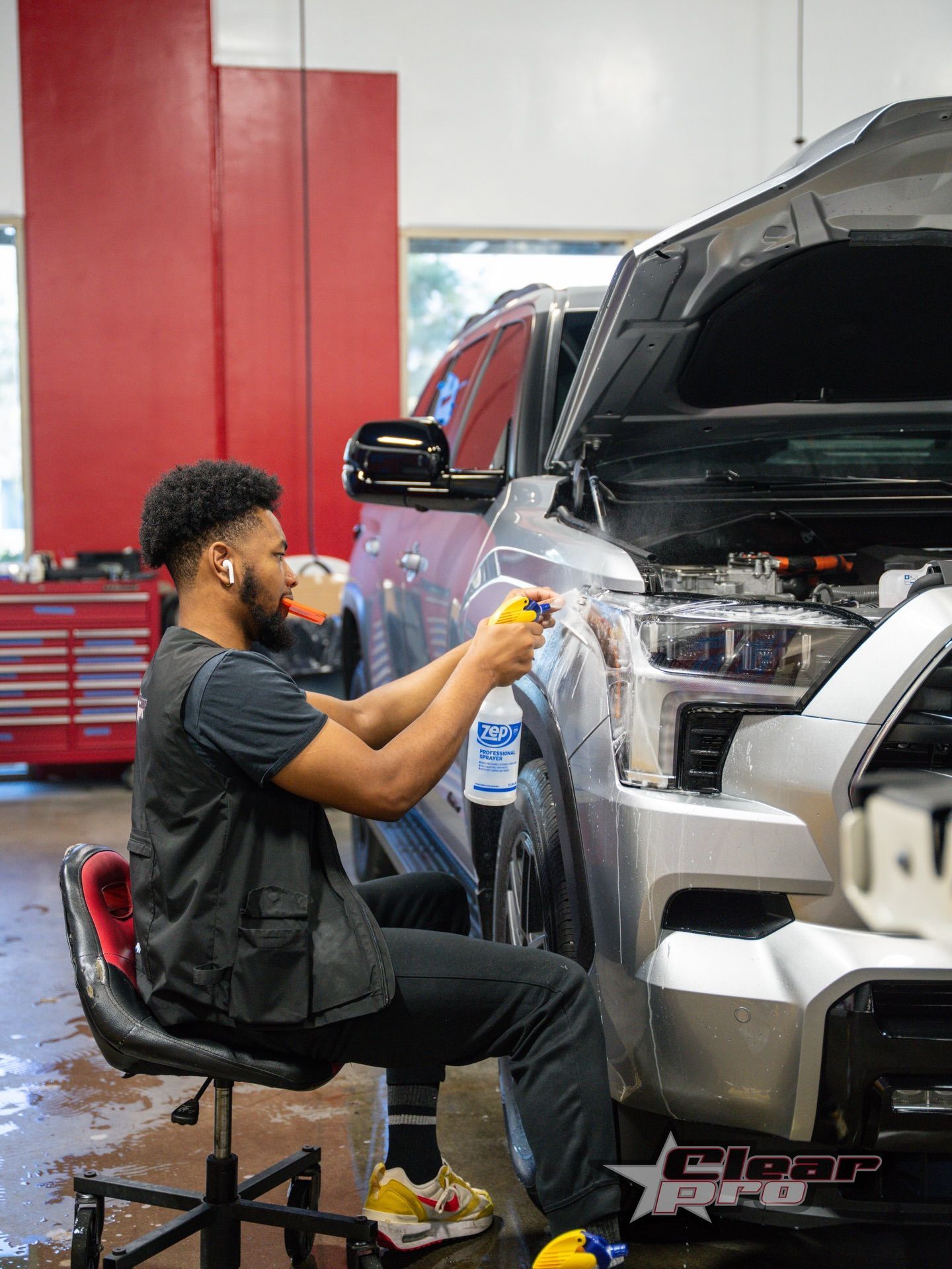 Mechanic polishing a black SUV in an auto shop, with the hood open and a red tool cabinet nearby.