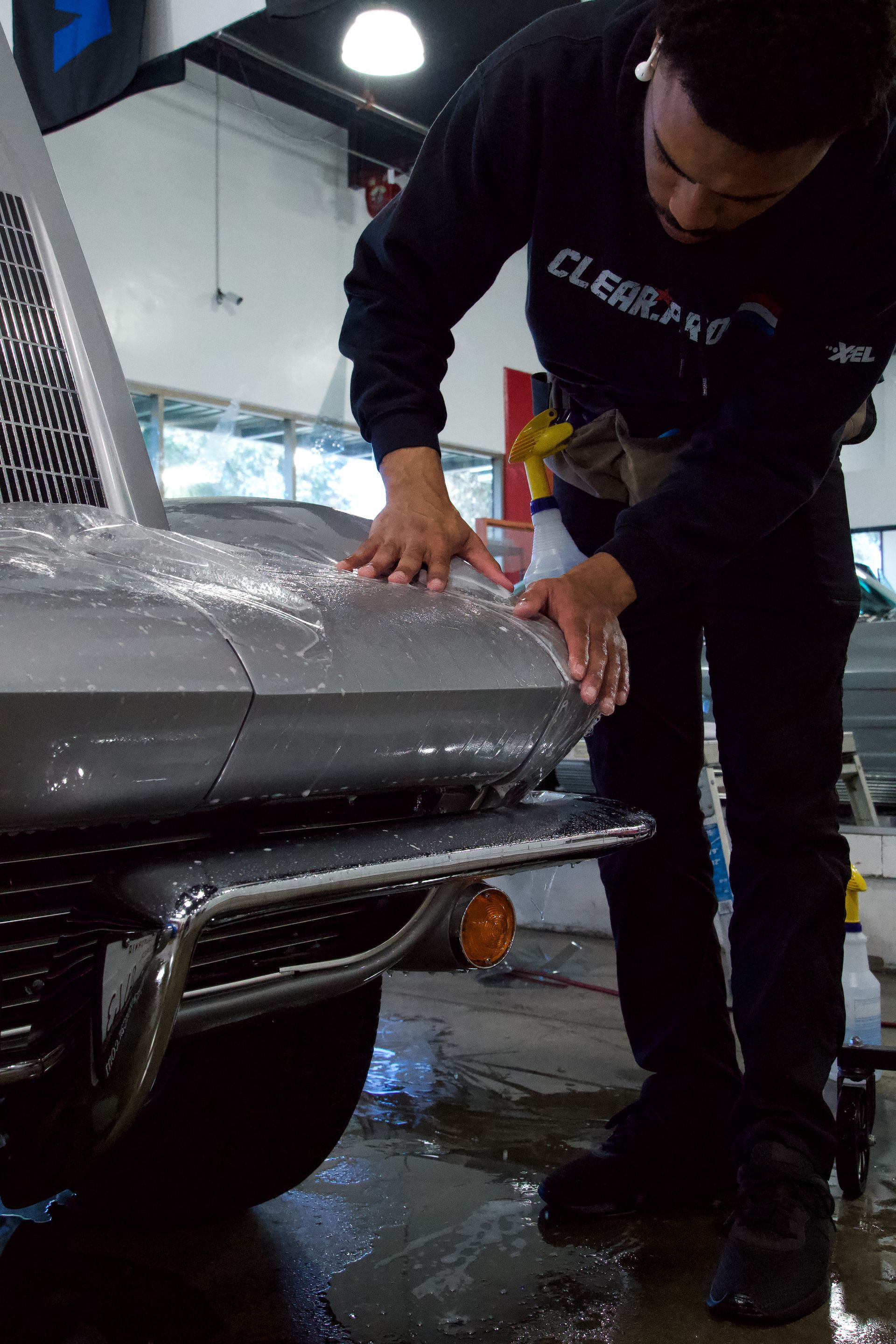 Person applying a protective film to the front of a silver car; spraying water.