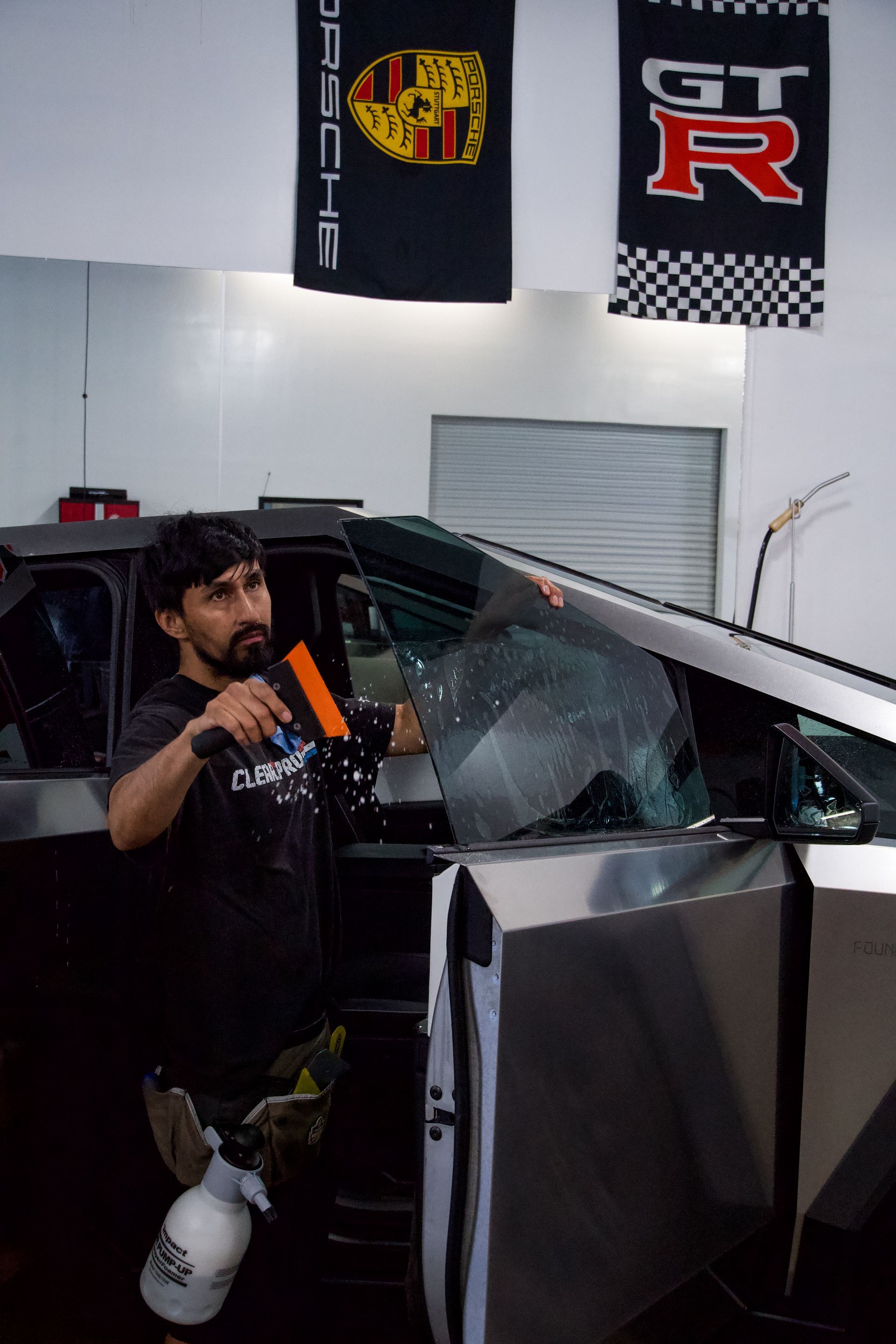 A man is applying window tinting to a car in a garage.