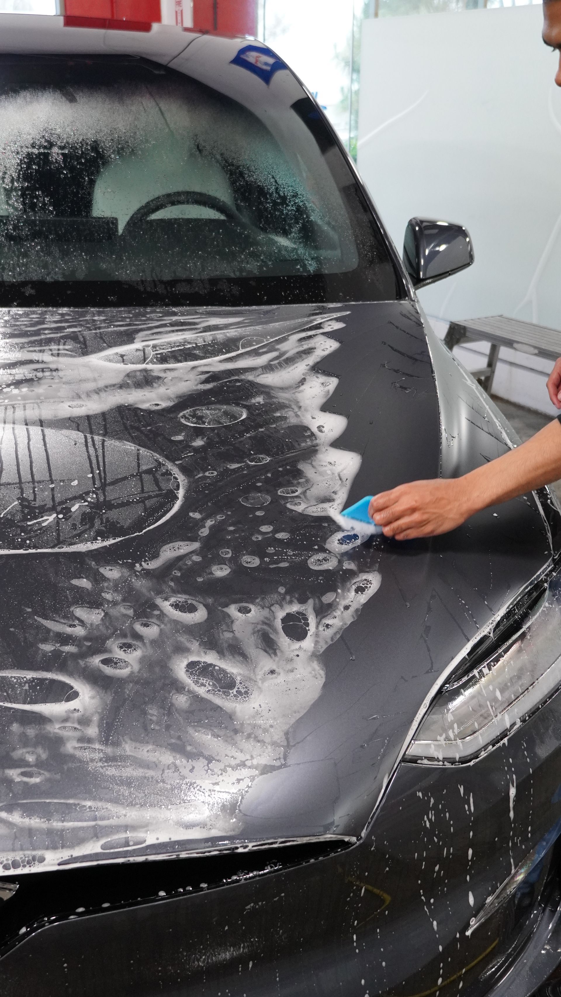 A person is cleaning the hood of a car with a sponge.