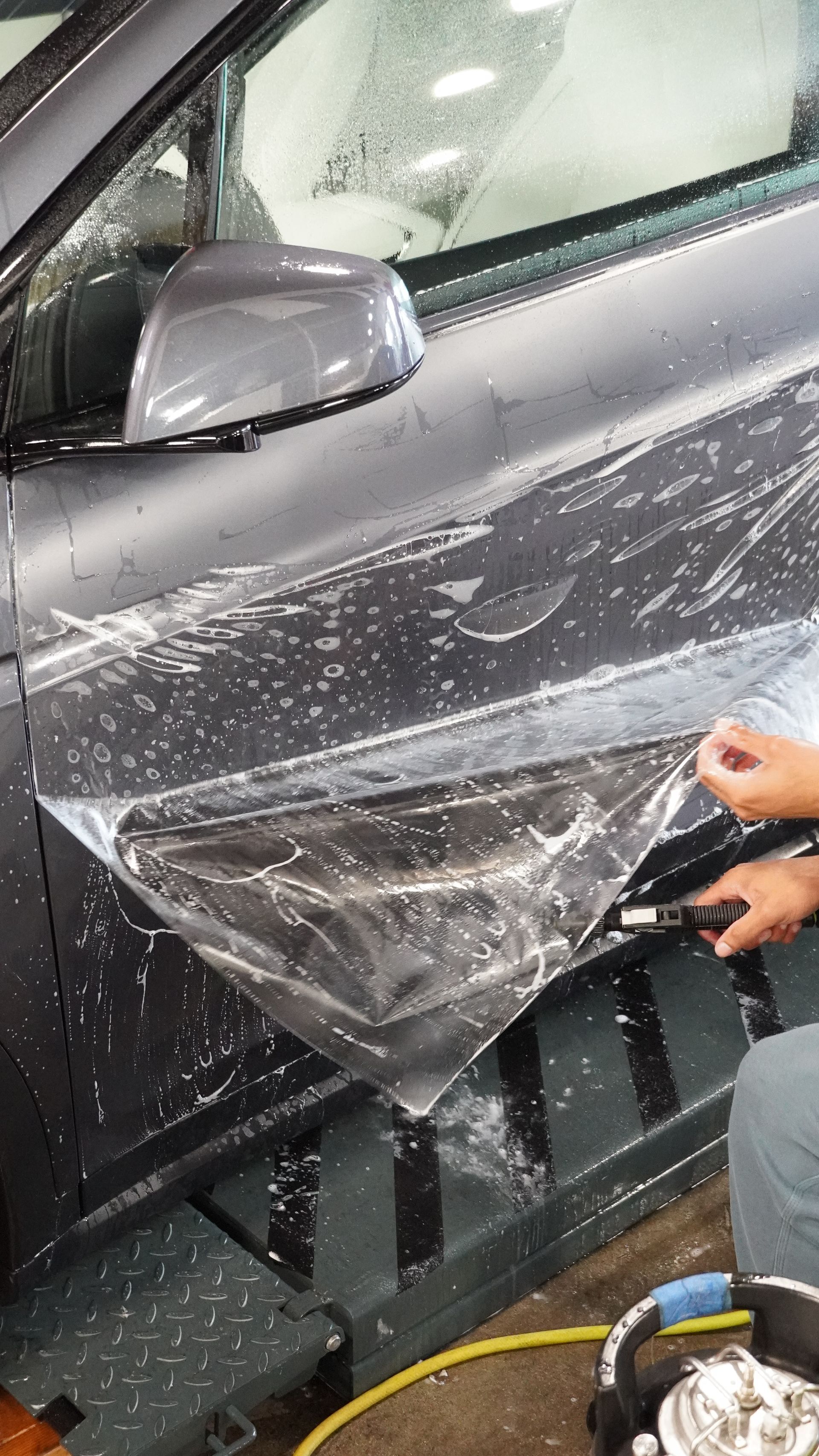 A person is applying a protective film to the side of a car.