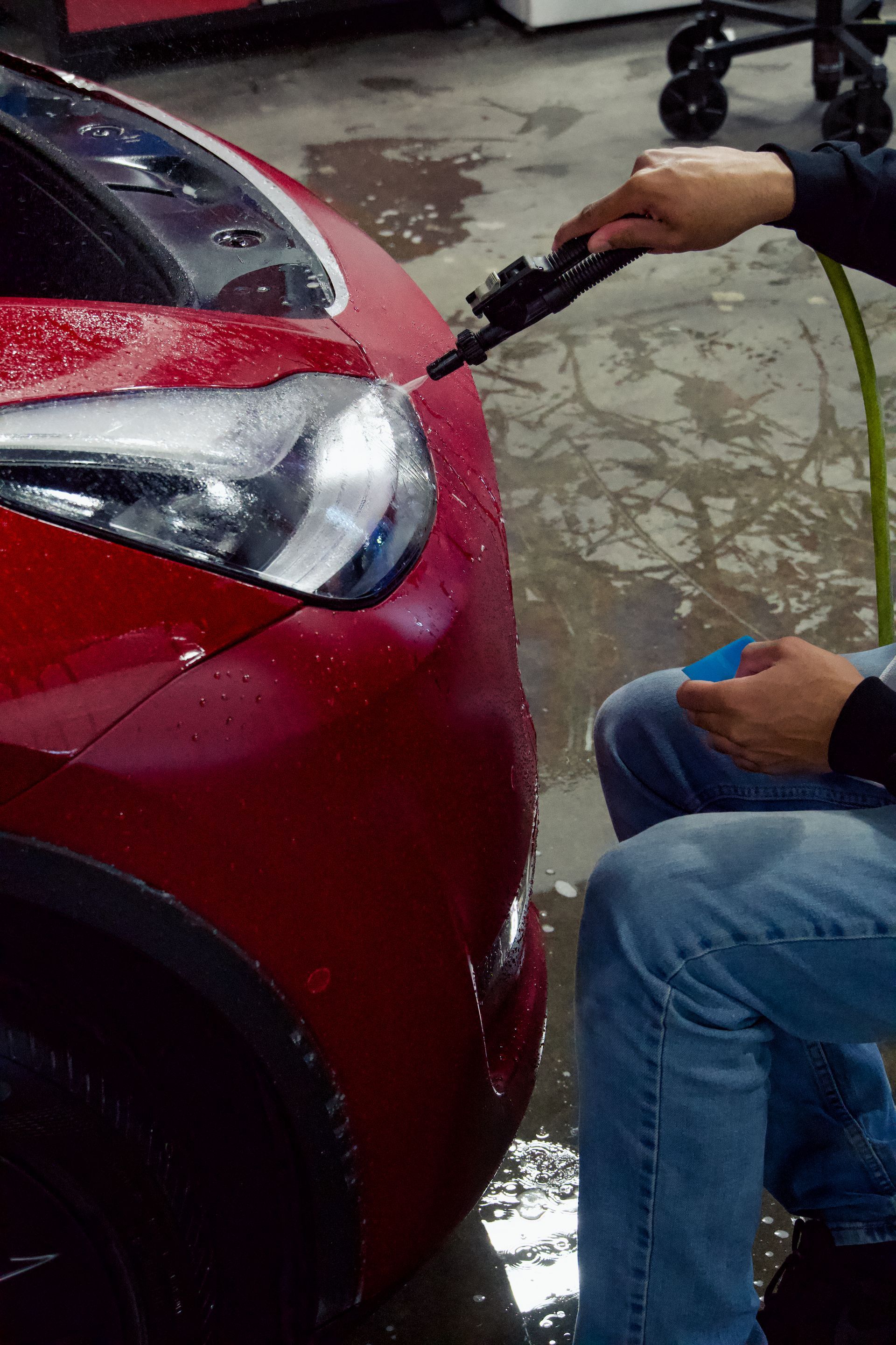 A person is washing a red car with a hose.