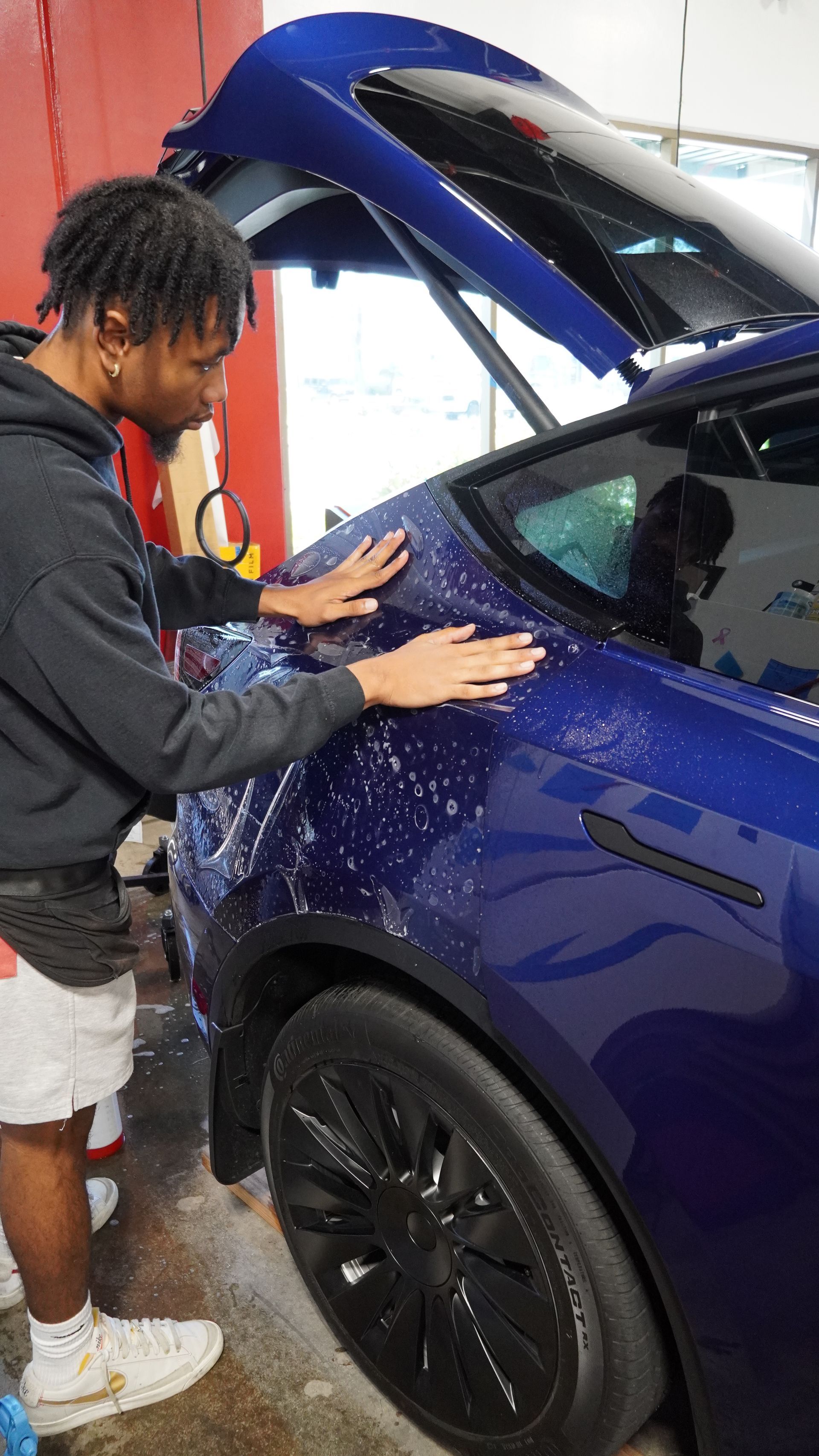 A man is wrapping a blue tesla model y with a wrap.