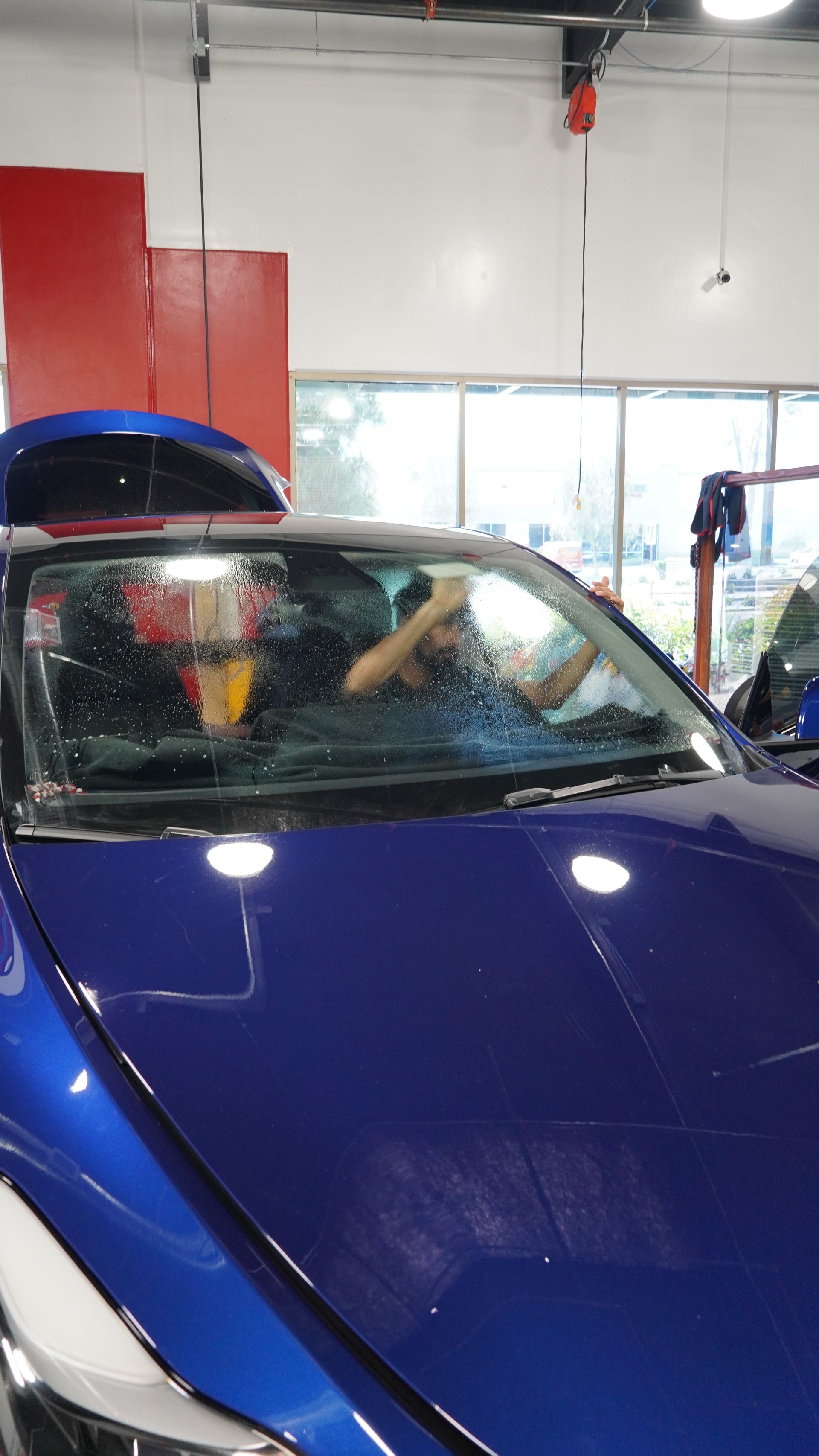 A man is sitting in the driver 's seat of a blue car in a garage.