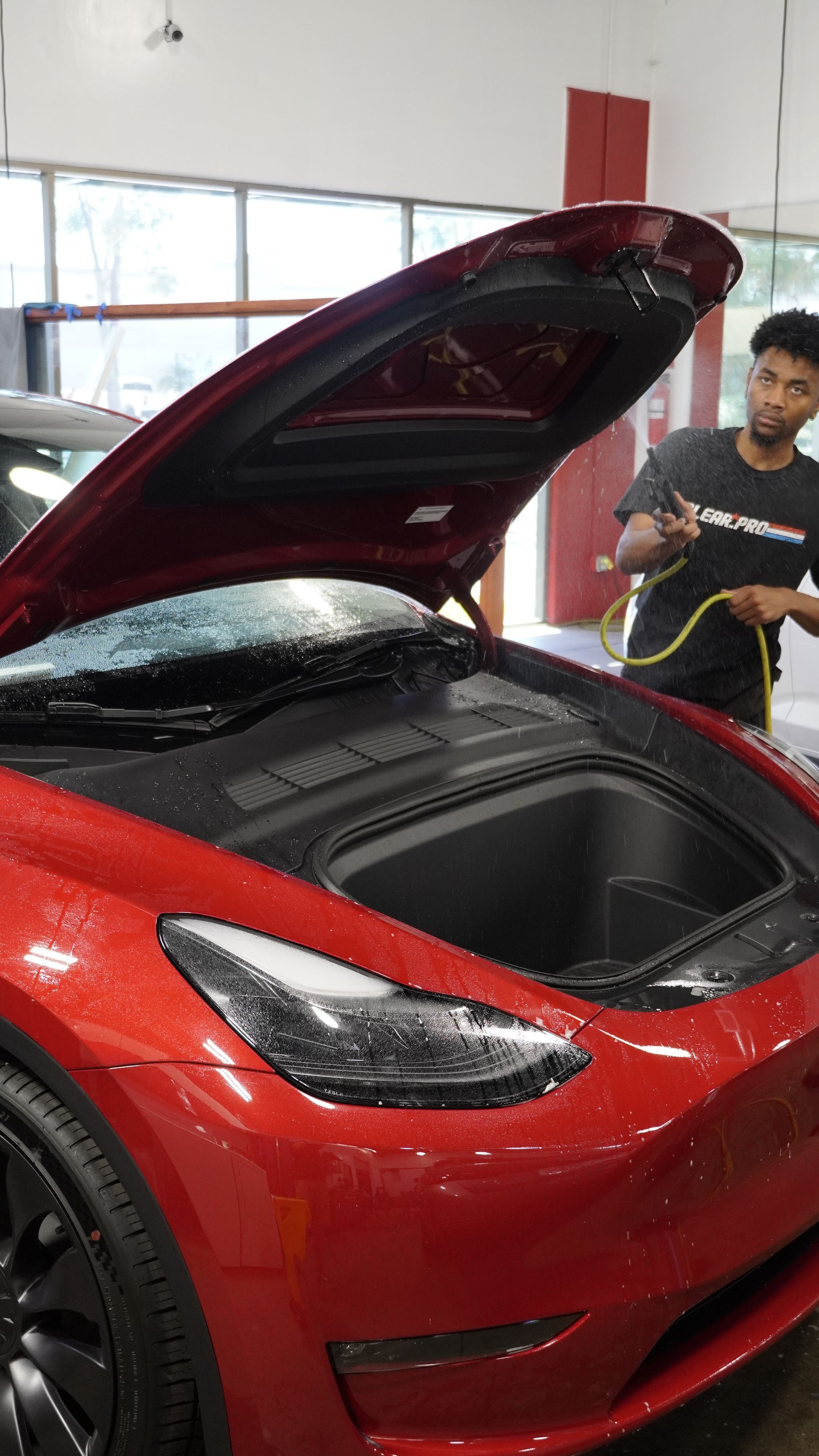 A man is cleaning the hood of a red tesla model 3.
