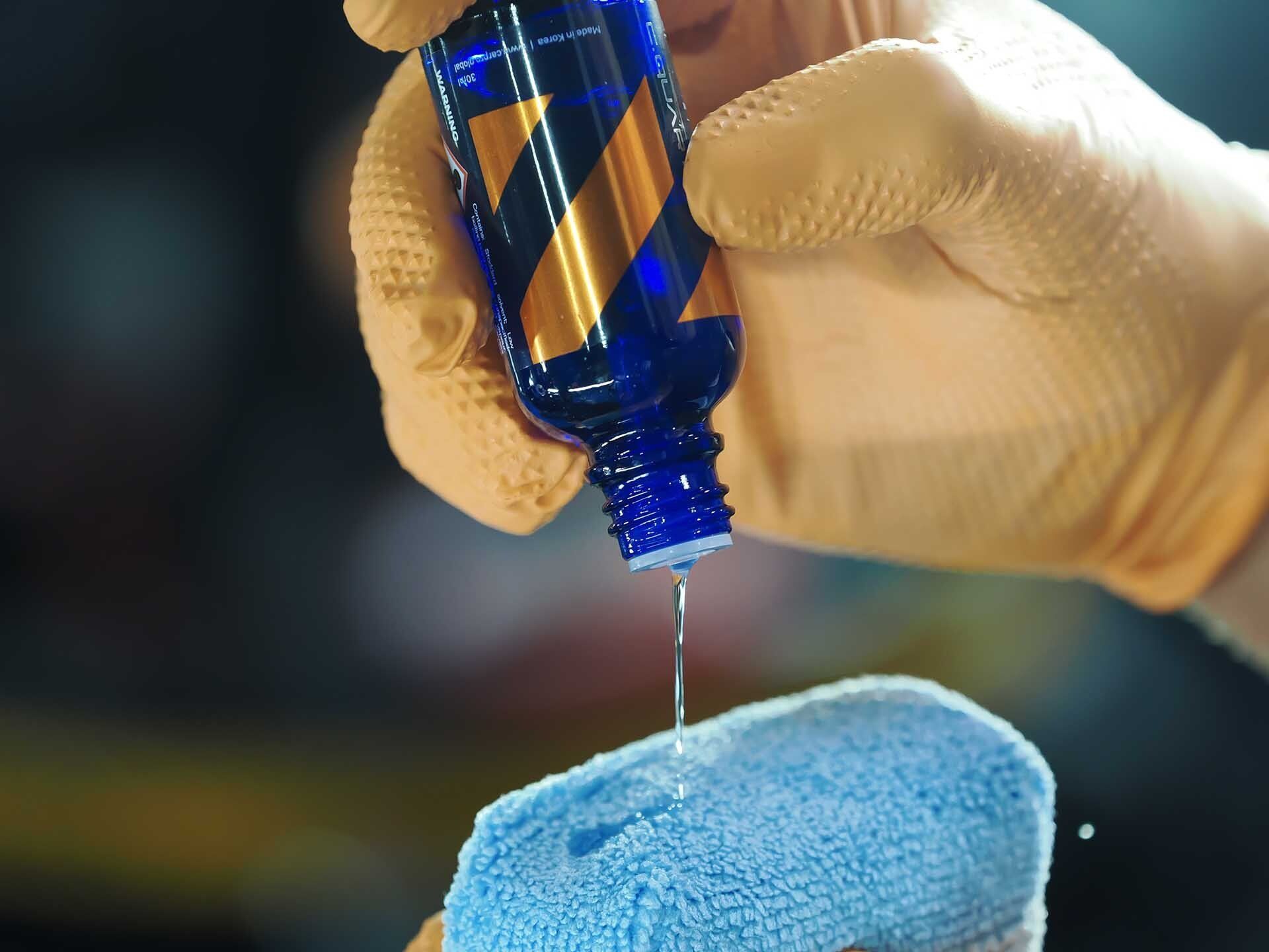 A person is pouring liquid from a bottle onto a sponge.