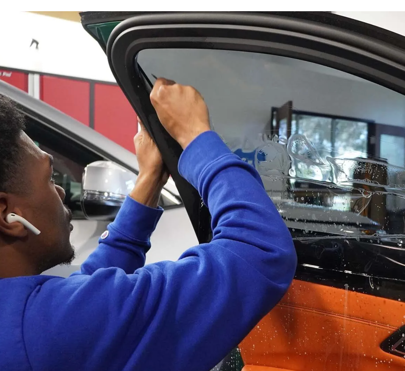 A man in a blue sweatshirt is working on a car