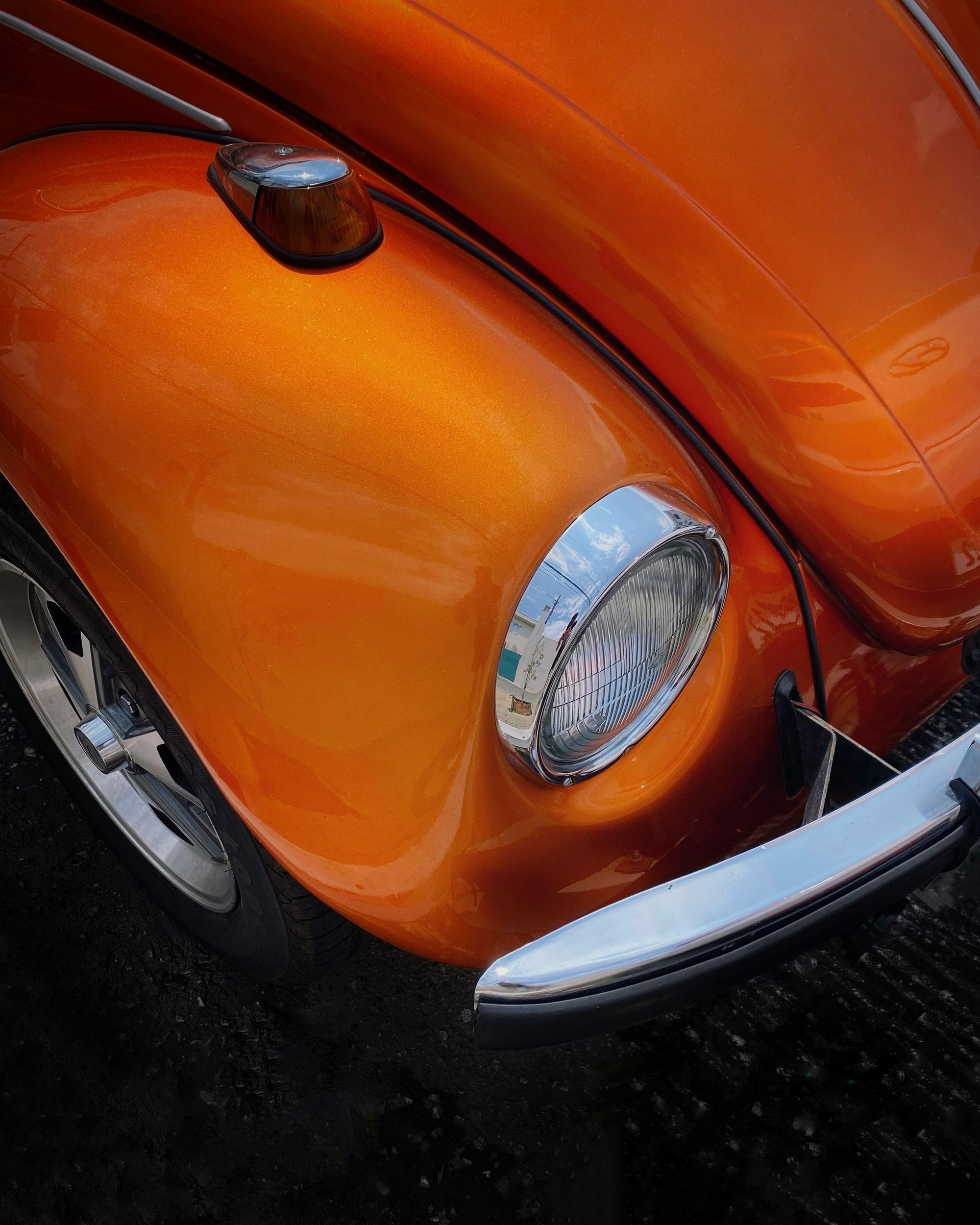 A close up of an orange car with a chrome headlight