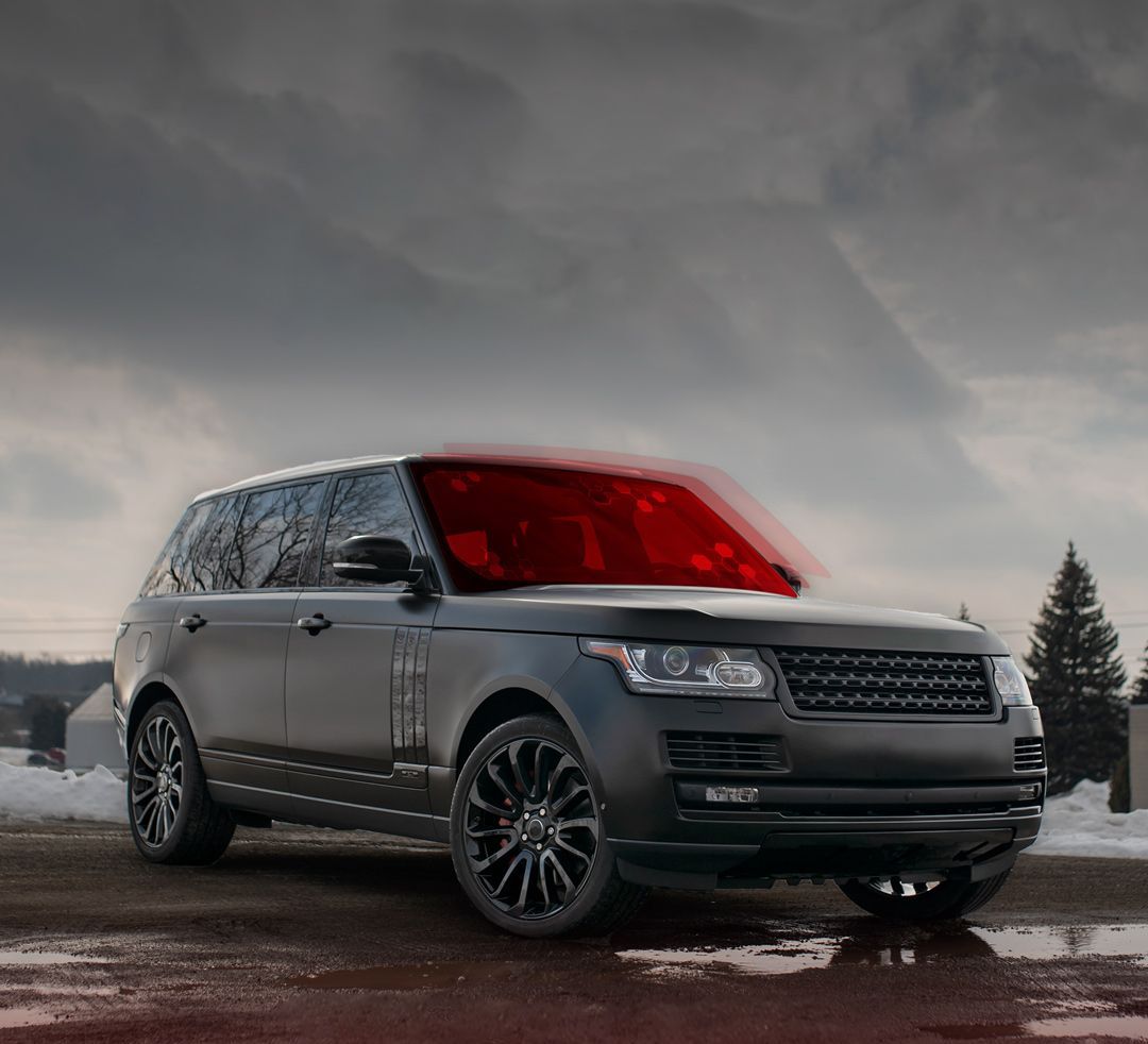 Black Range Rover parked on a wet surface with a red windshield, overcast sky.