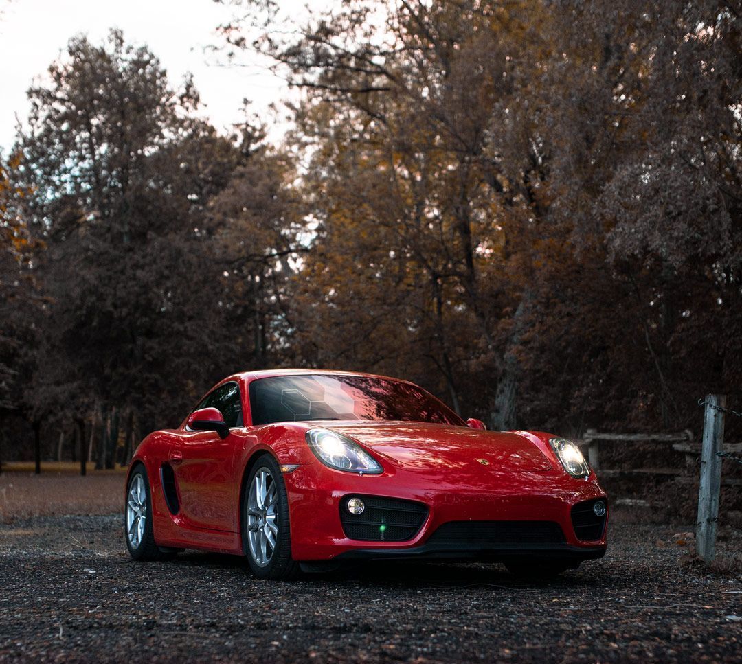 Red sports car parked on gravel, trees in background.
